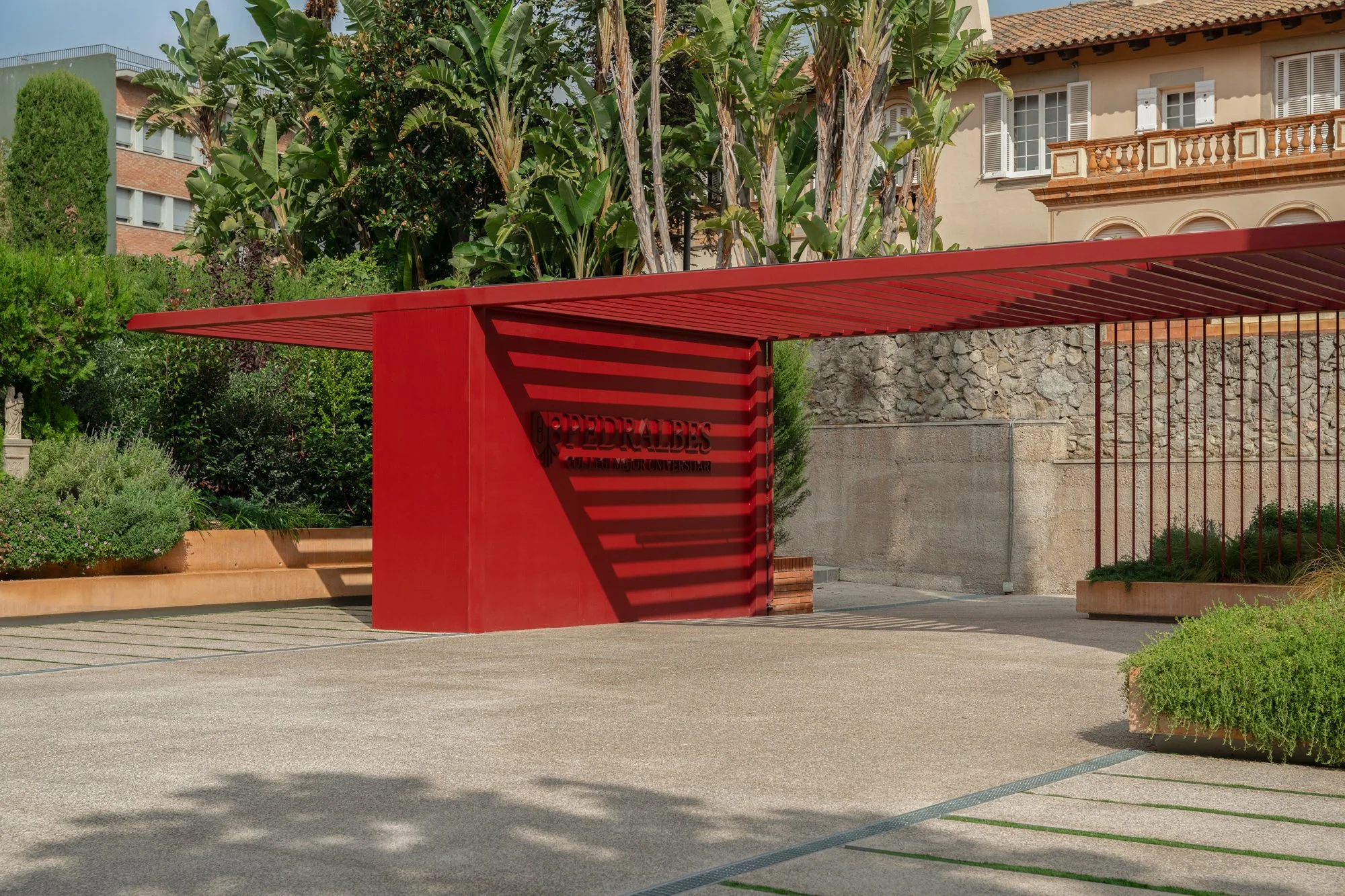 Estructura de ingreso al edificio, con un cartel que dice 'PEDREGALES' y sombra de líneas horizontales creadas por el techo de la estructura