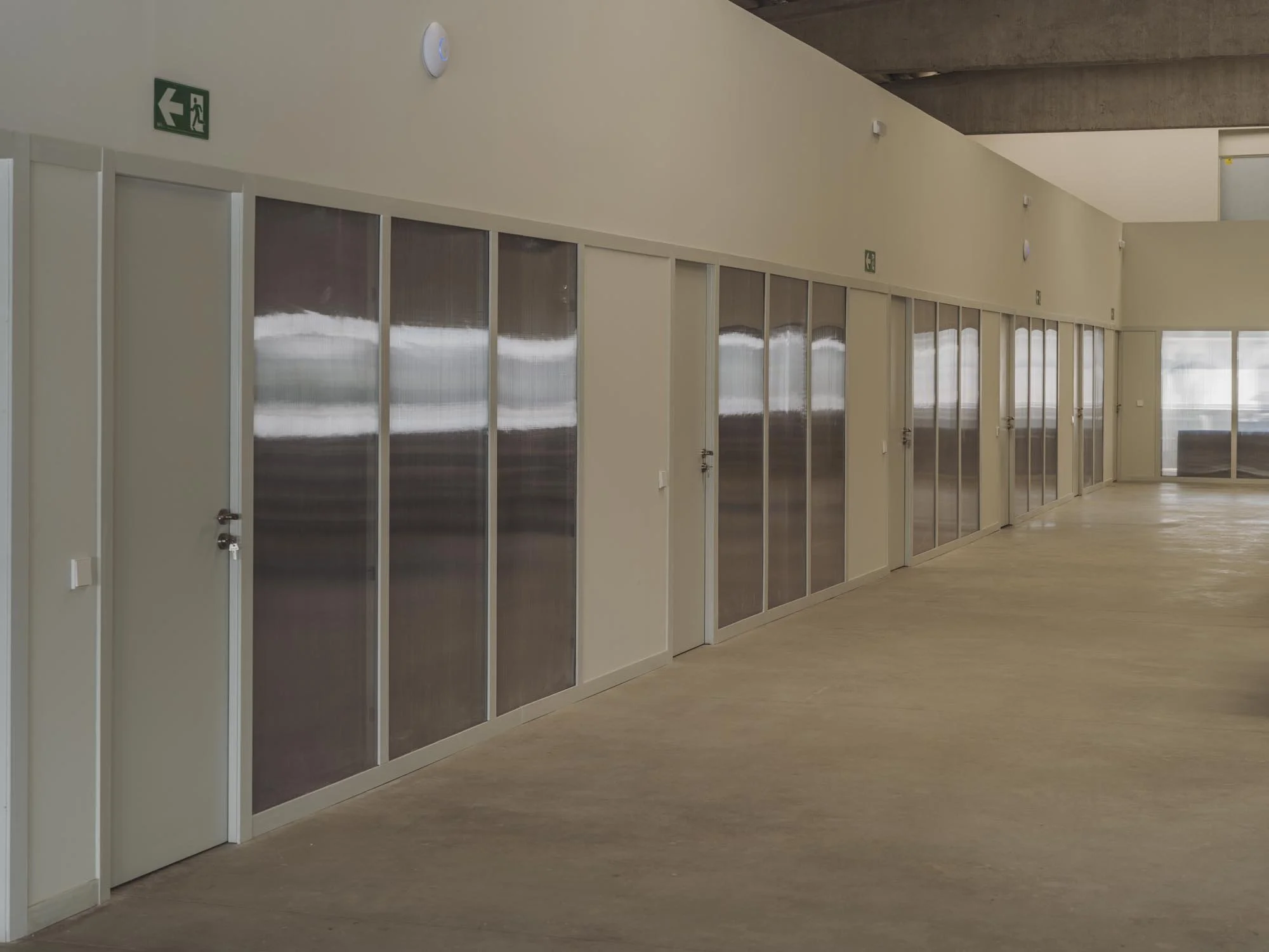 Pasillo con puertas de vidrio y señal de salida de emergencia en la pared