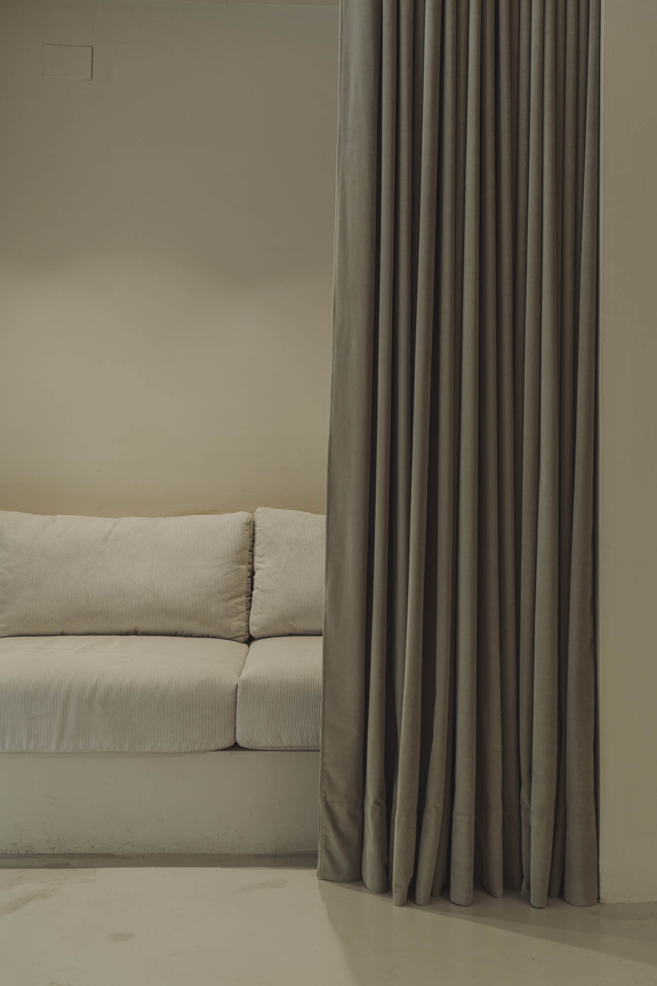 Sala con sofá beige y cortinas gruesas de color gris en una pared de color claro.