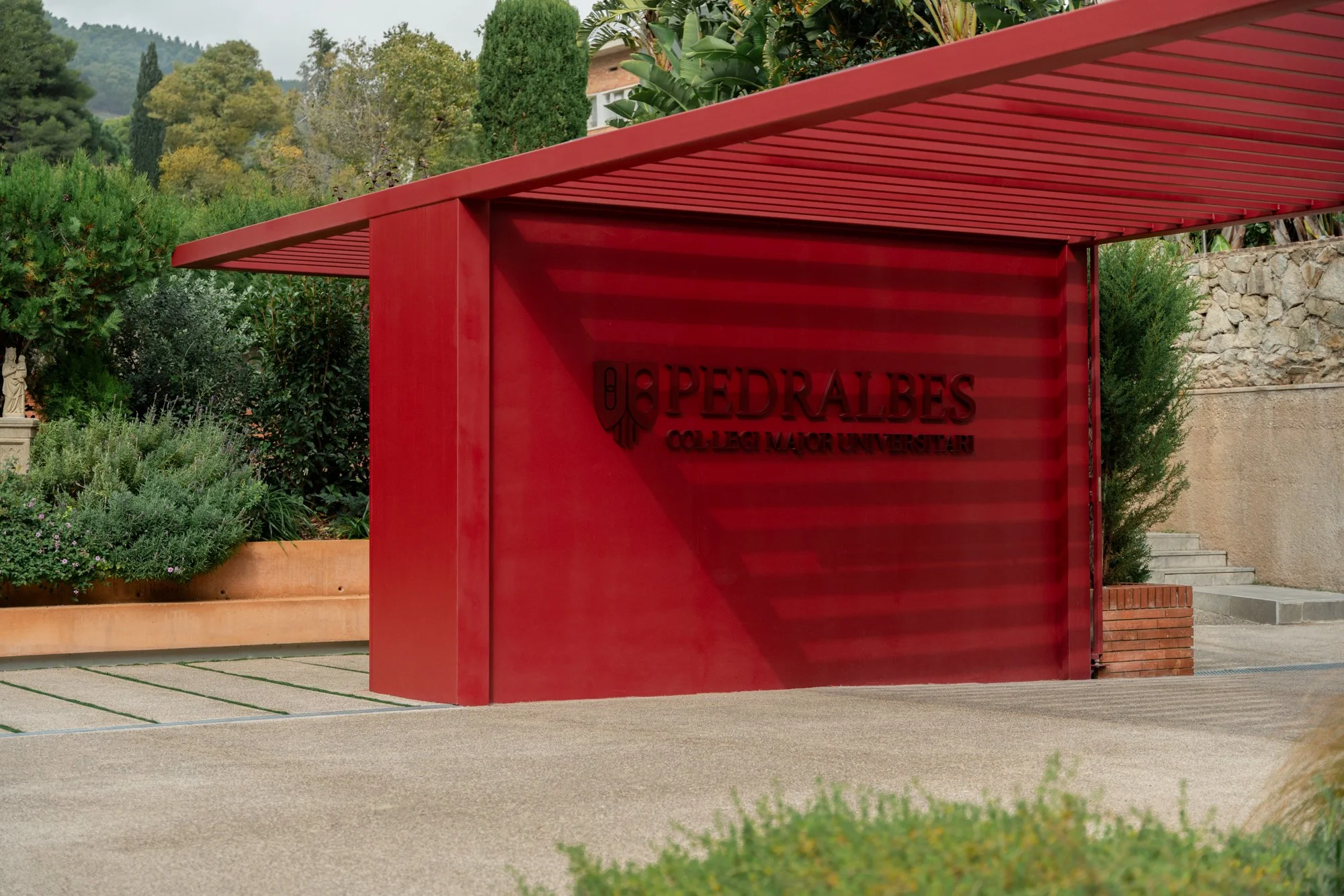 Entrada al colegio mayor universitario Pedralbes, con una estructura moderna de color rojo y vegetación alrededor.