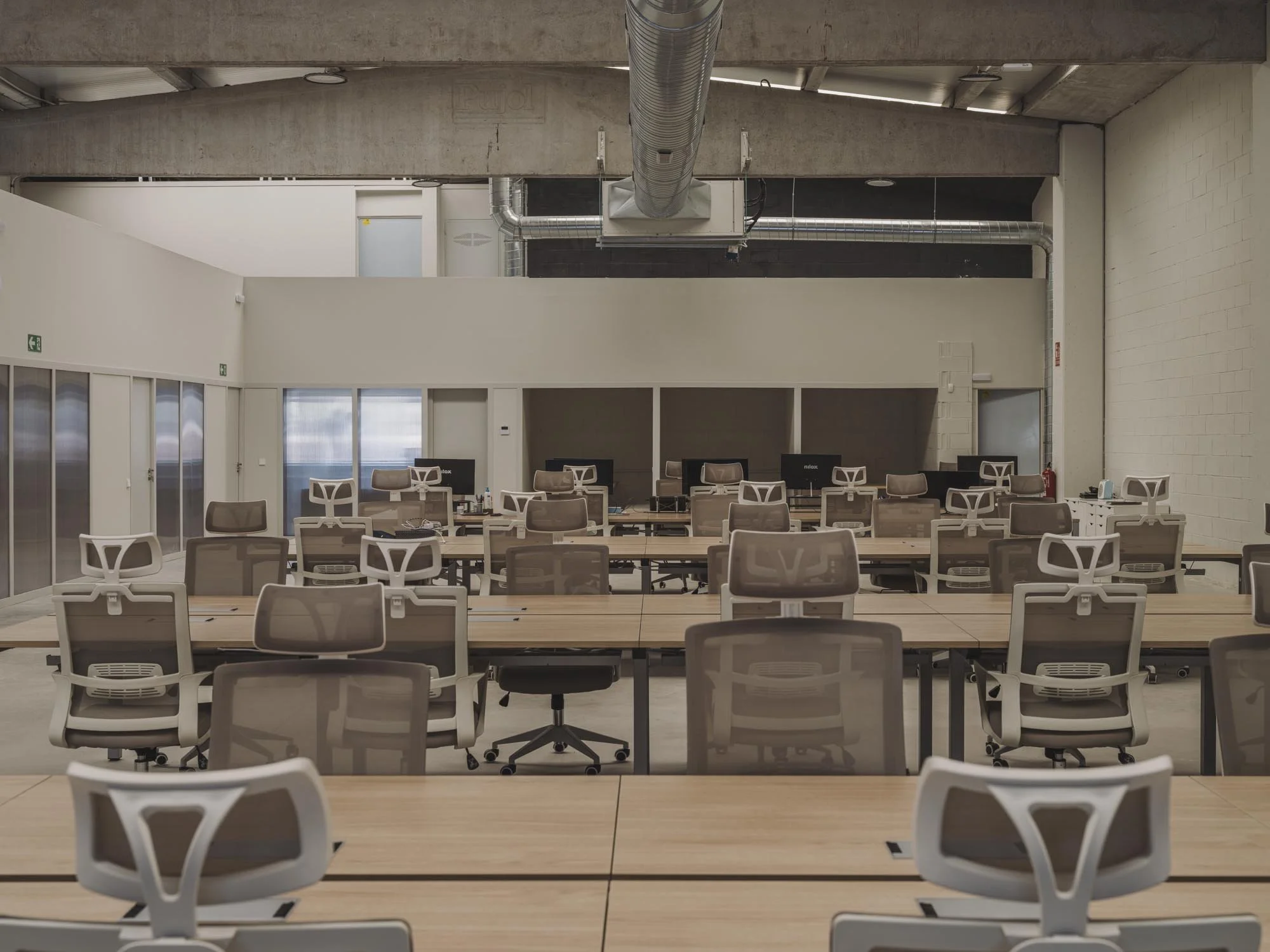 Oficina moderna con varias mesas de madera y sillas ergonómicas, computadoras y equipo de oficina en un espacio amplio y bien iluminado.