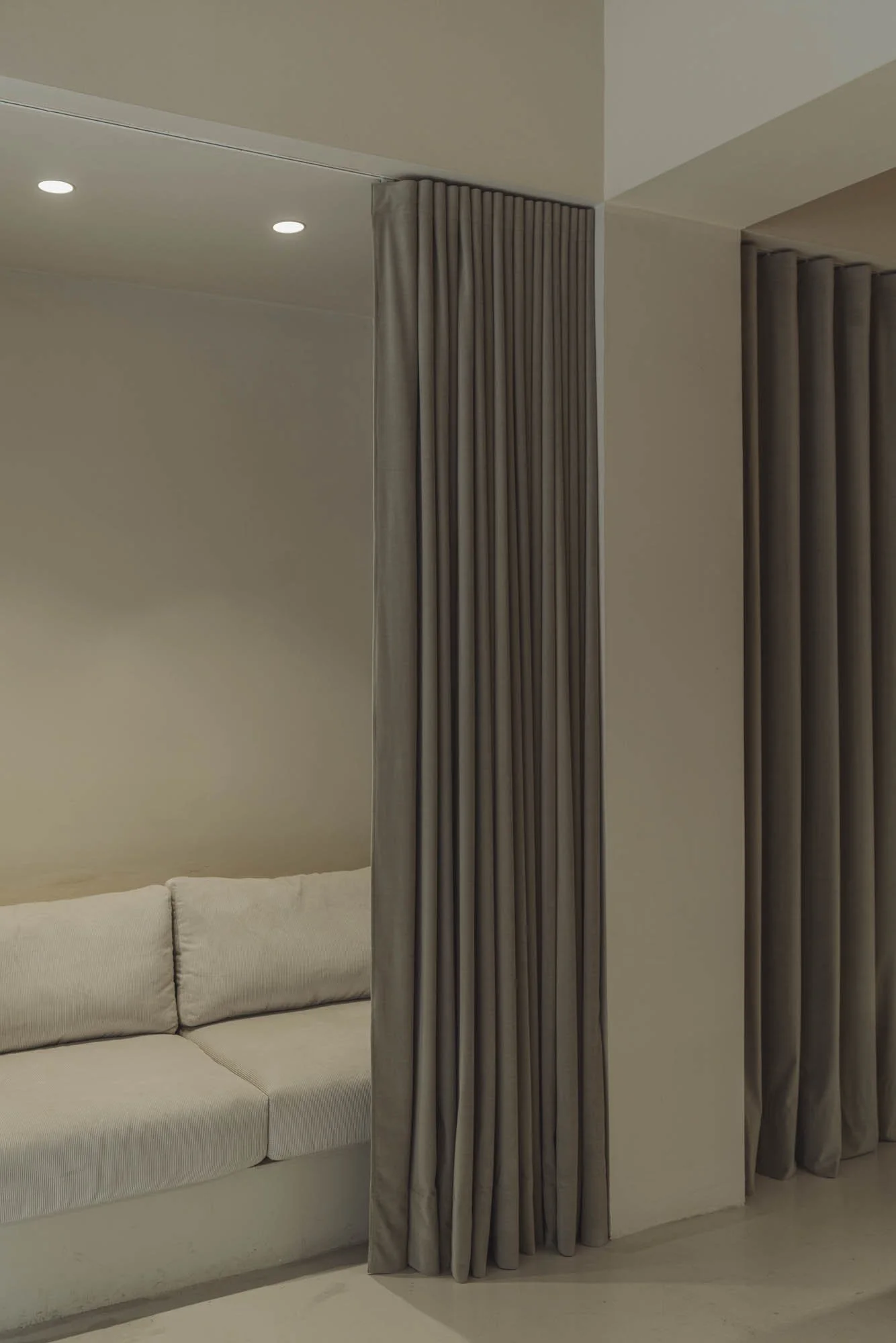 Cortinas grises en una habitación moderna con un sofá beige y luces empotradas en el techo.