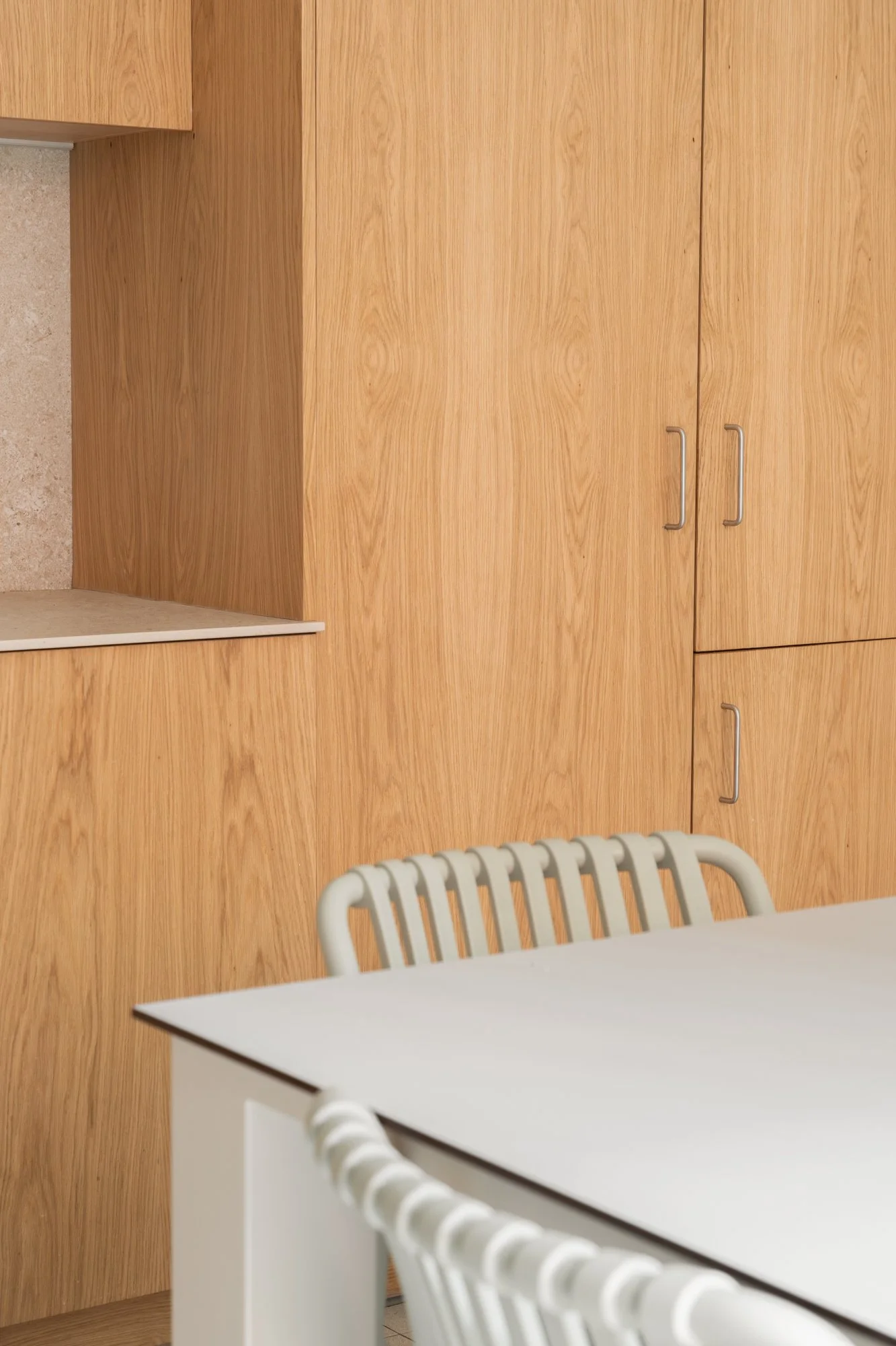 Muebles de cocina de madera con puertas y un área de desayunador, con sillas blancas que tienen respaldo de barras horizontales.