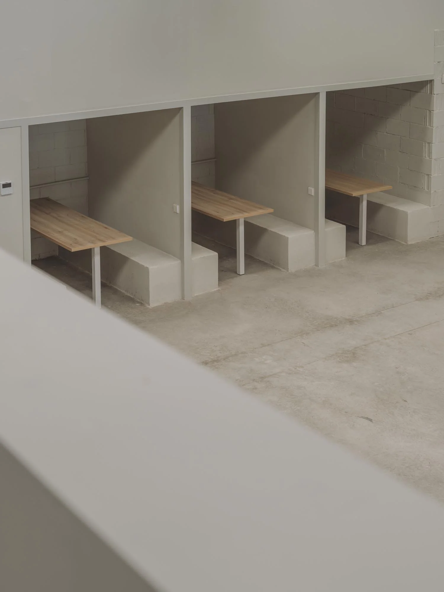 Imagen de cabinas de estudio con escritorios de madera y paredes de cemento, en un ambiente minimalista y moderno.