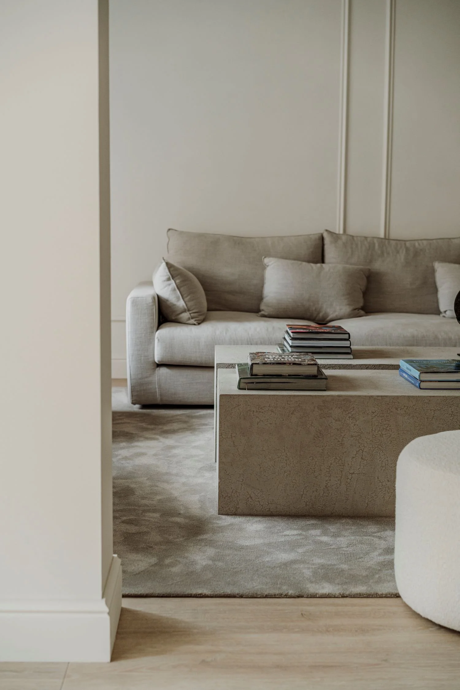 Salón elegante con sofá beige, cojines y mesas con revistas, decorado en tonos neutros y suelo de madera