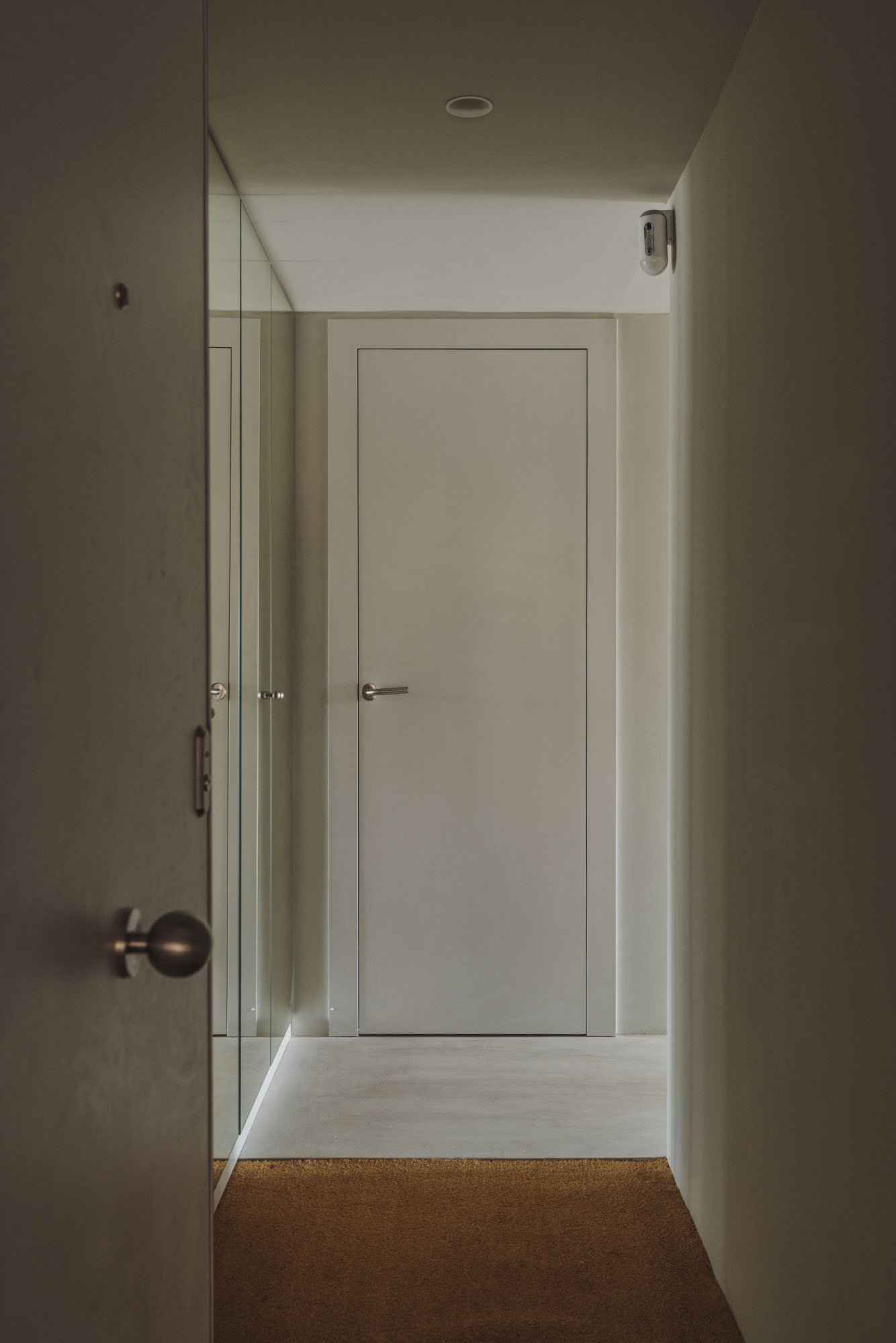 Pasillo con puerta cerrada, espejos en las paredes y una cámara de seguridad en la esquina superior derecha.