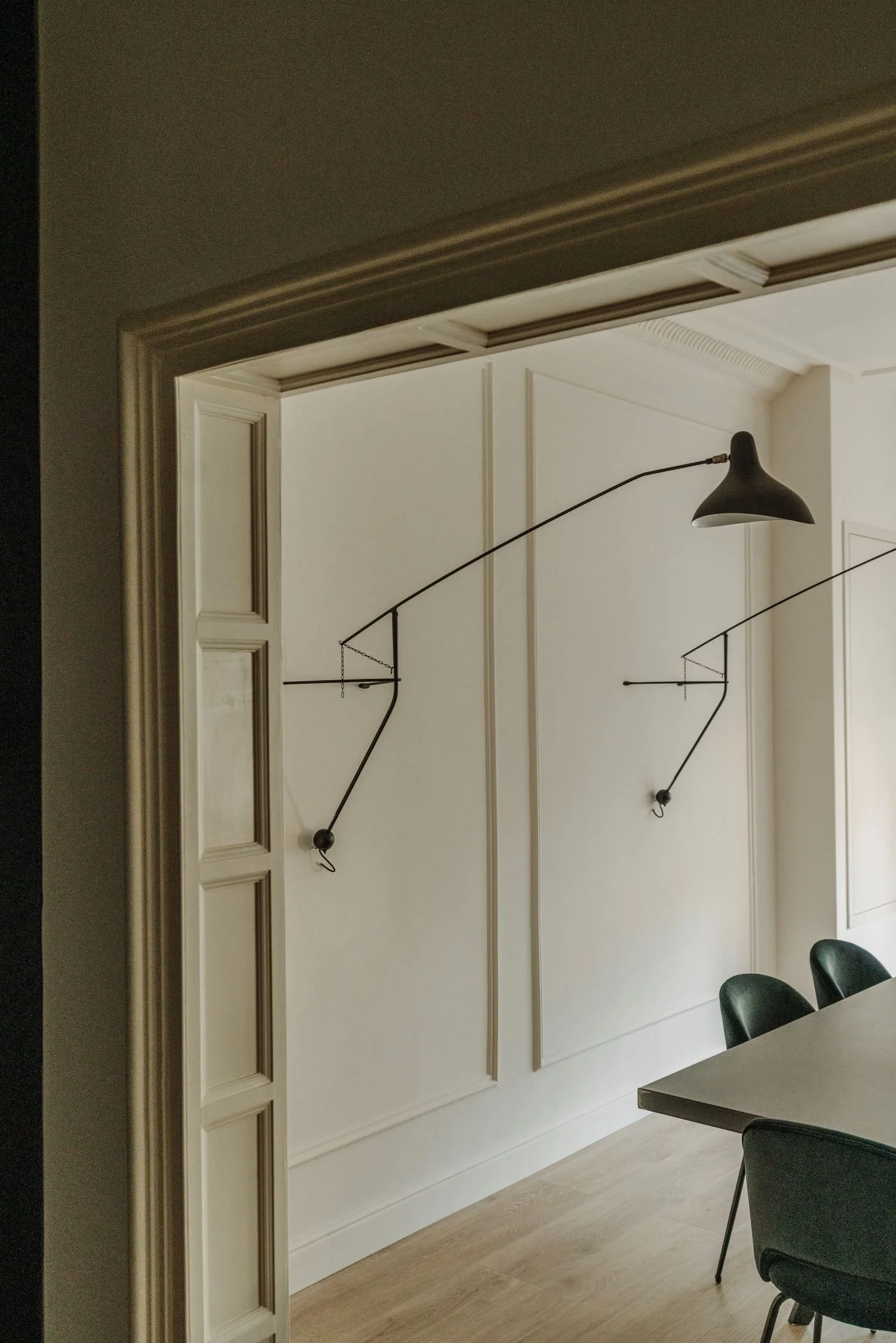 Sala moderna con paredes blancas, escritorio de madera y sillas verdes, dos lámparas de diseño en la pared, una de ellas con brazo articulado.