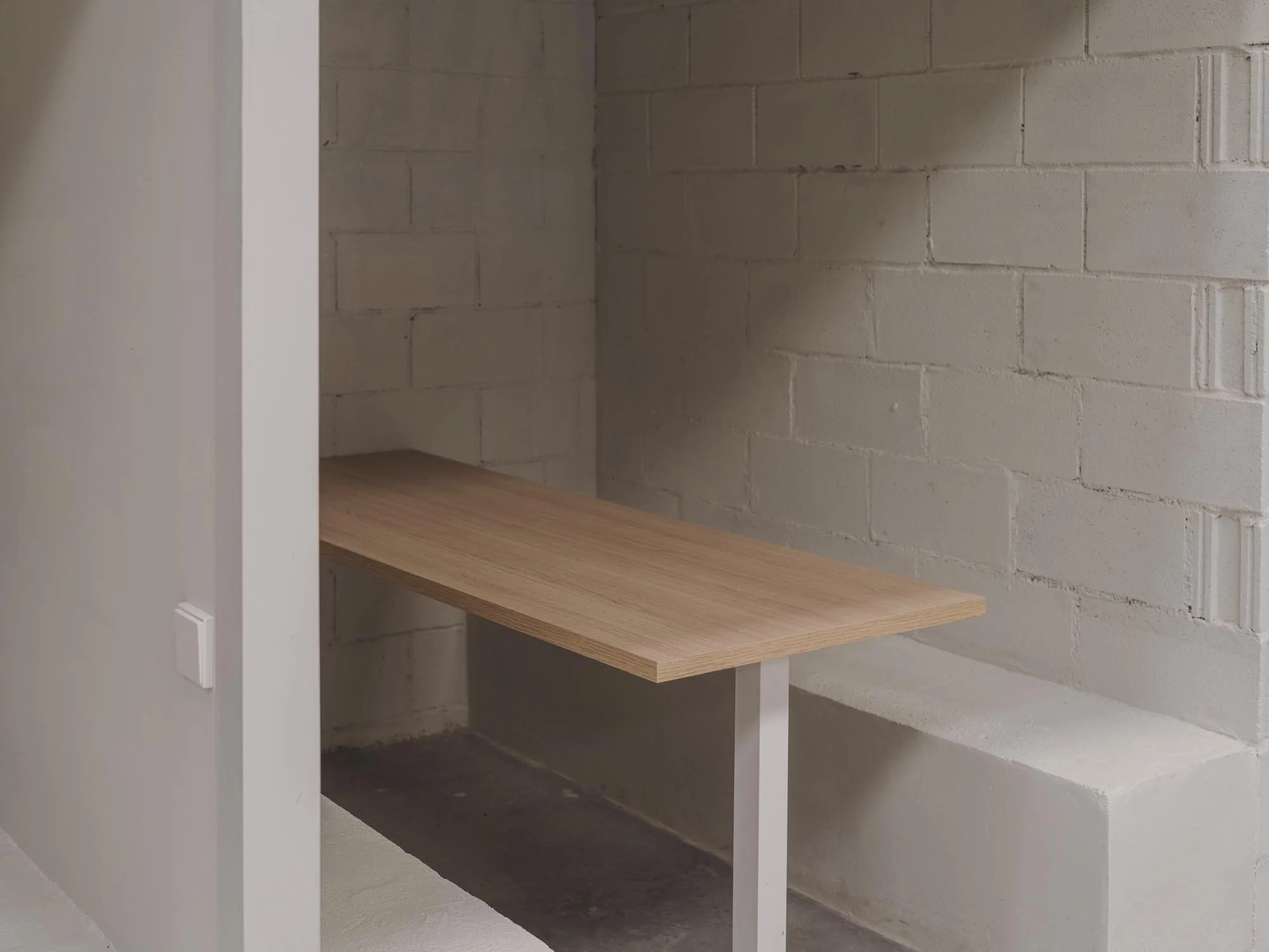 Una esquina con paredes de ladrillo pintadas de blanco, y un estante de madera sobre una estructura de metal blanco.