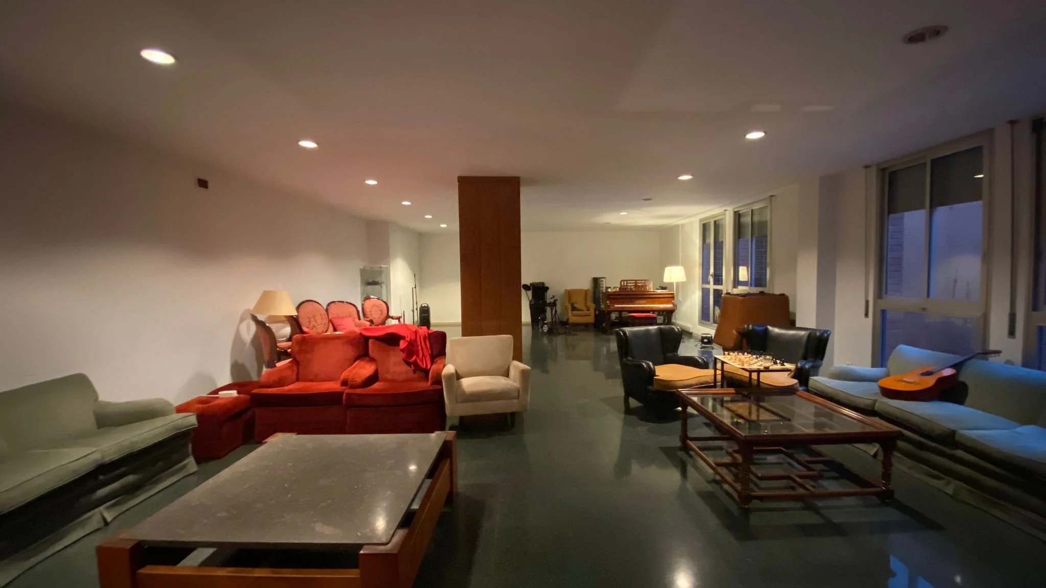 Sala de estar con sillones de varios colores, una mesa y una guitarra en un ambiente con ventanas grandes y luz suave.