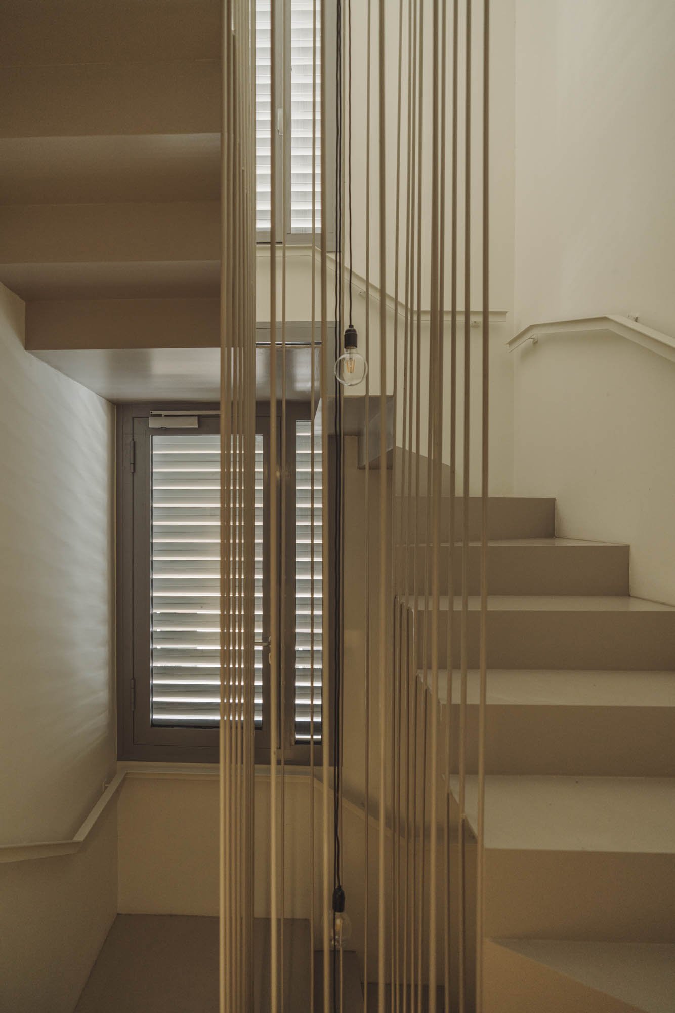 Escalera interior con barandilla de madera y ventanas con persianas en tonos claros