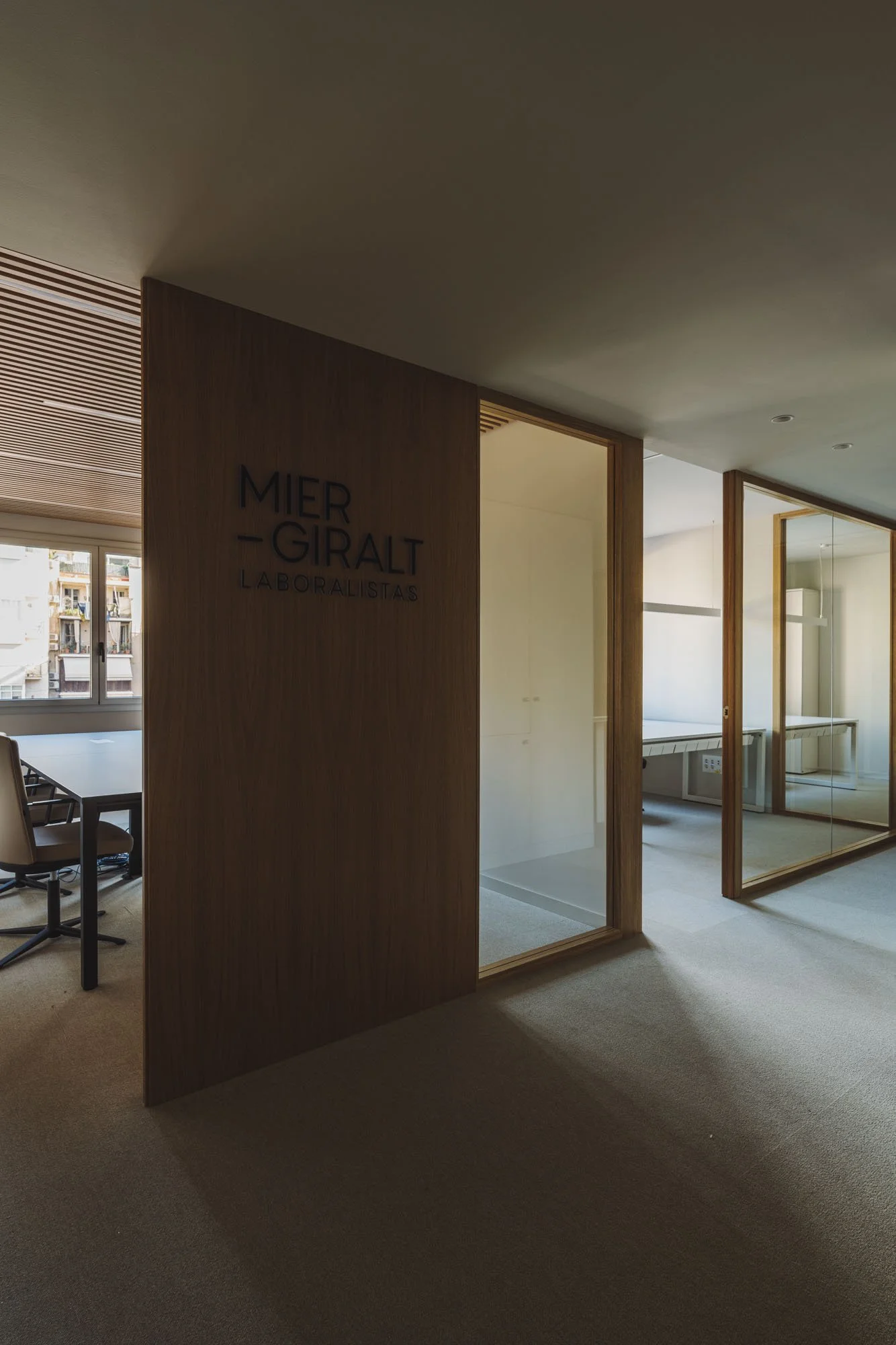 Galería de oficinas con paredes de vidrio, nombre en madera 'Mier-Giralt Laboralistas' en una de ellas, mobiliario de oficina visible al fondo.