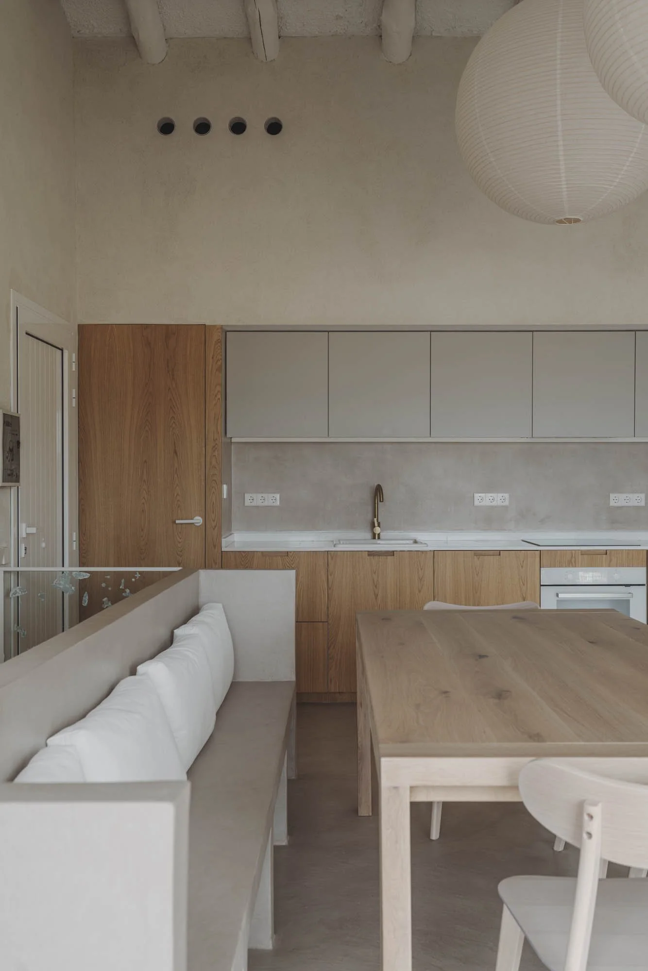 Cocina moderna con gabinetes de madera, luminarias de papel y mesa de madera en un interior minimalista.