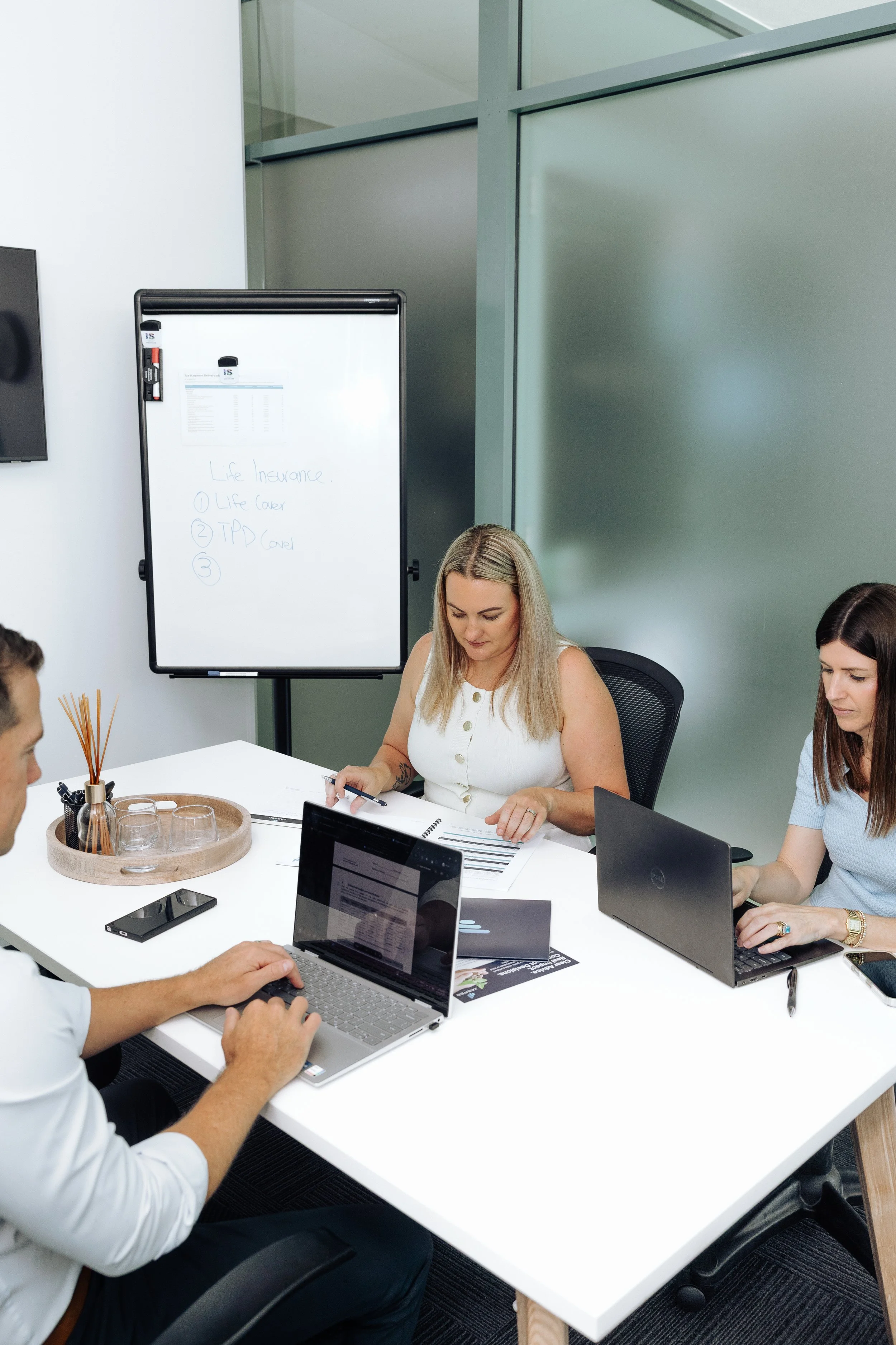 People in a meeting room working on laptops with a whiteboard in the background displaying handwritten notes about life insurance.