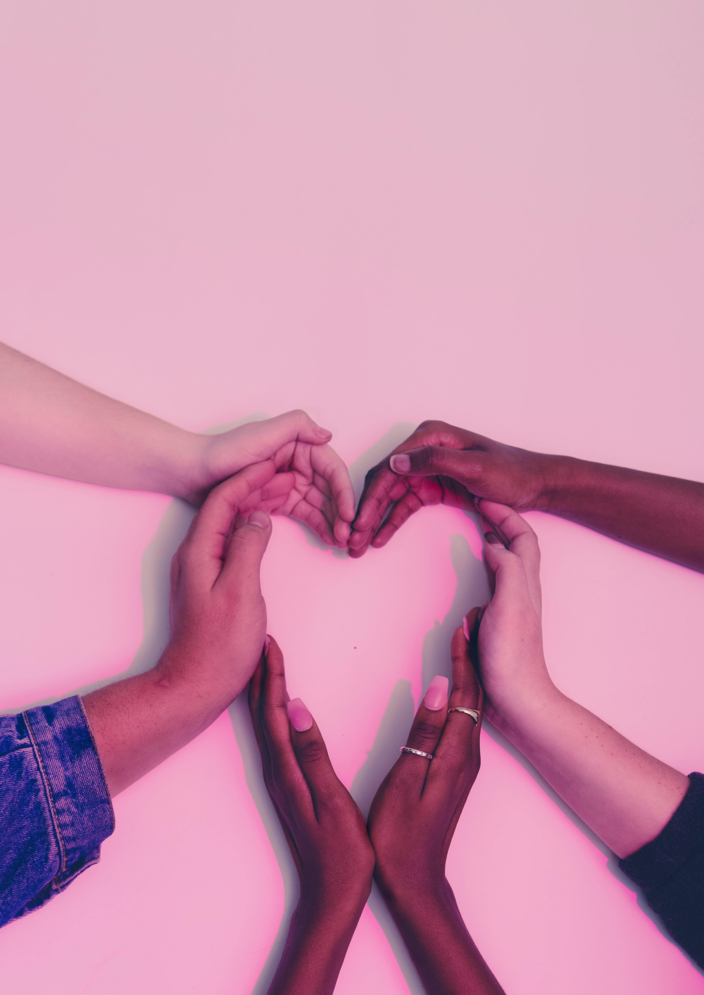 Multiple hands of different skin tones forming a heart shape on a pink background.