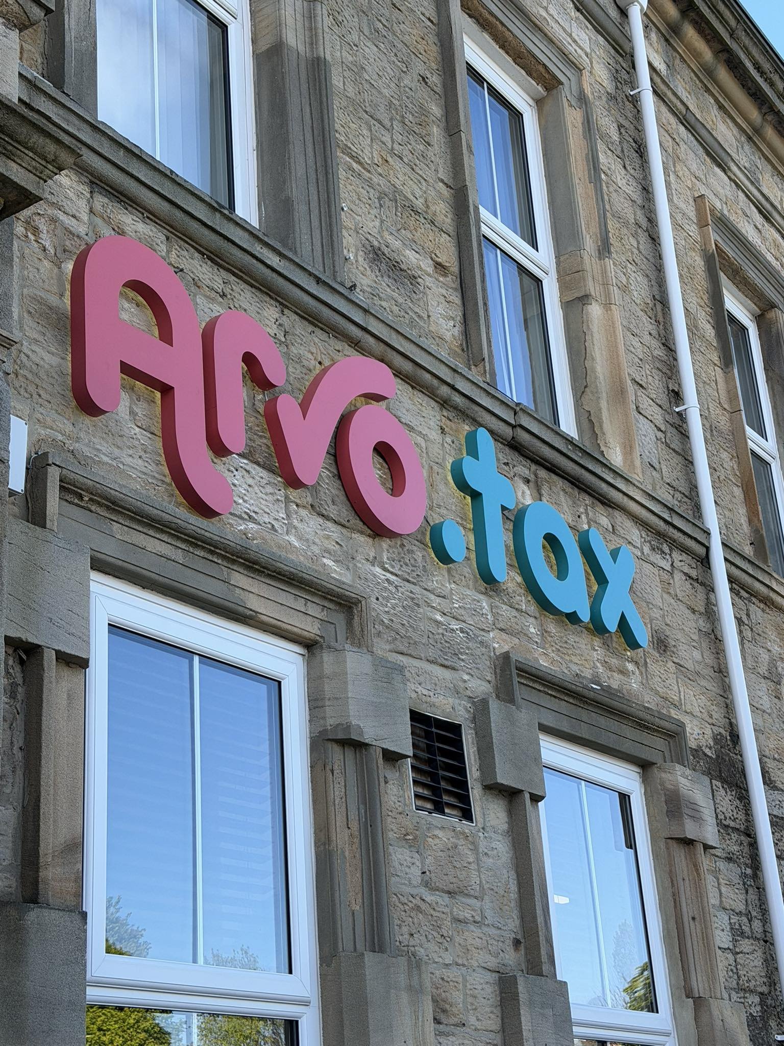 Close-up of a building with a stone facade and four large windows; a neon sign with pink and blue letters reading 'HVO' is mounted on the building.