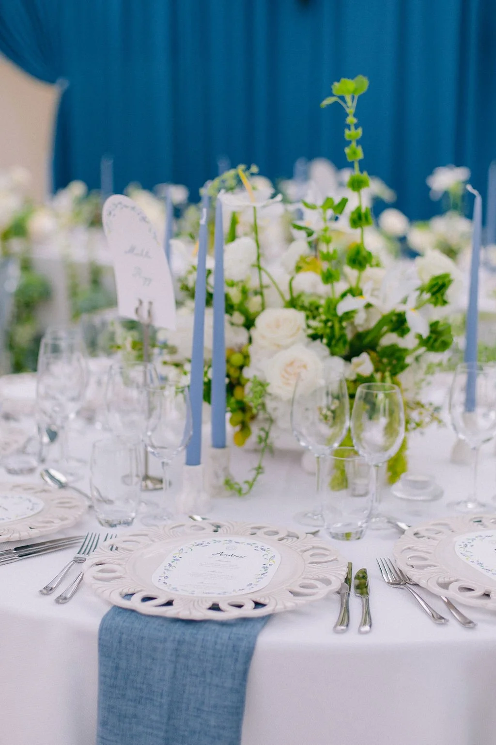 Elegant table setting with white and blue decor, floral centerpiece, and place cards for a wedding or special event.