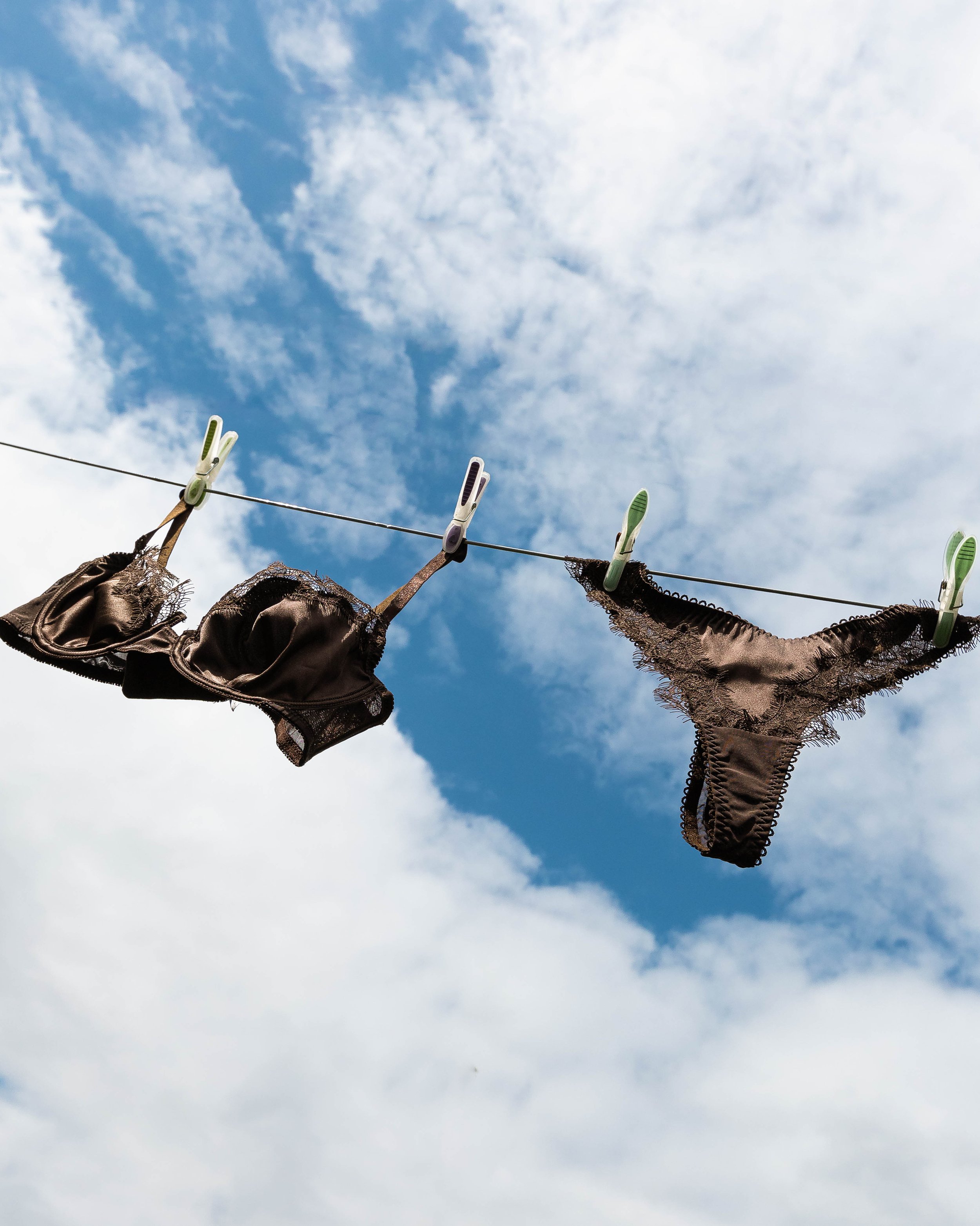 Black lingerie hanging on a clothesline with clothespins against a blue sky with clouds.