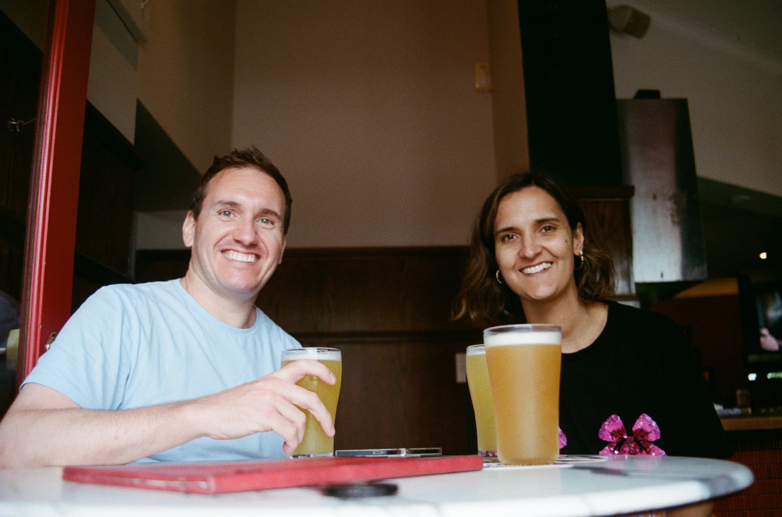  35mm photograph of a man in a blue shirt and a woman with dark hair in pub with pints in front of them smiling at the photographer.  