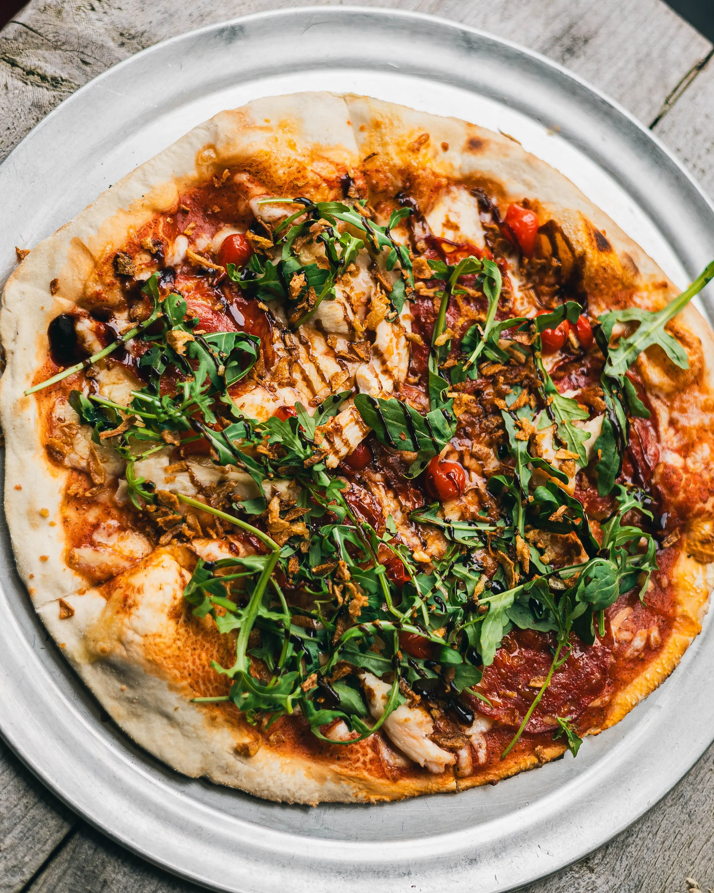 Pizza with arugula, cherry tomatoes, crispy onions, and drizzled sauce on top