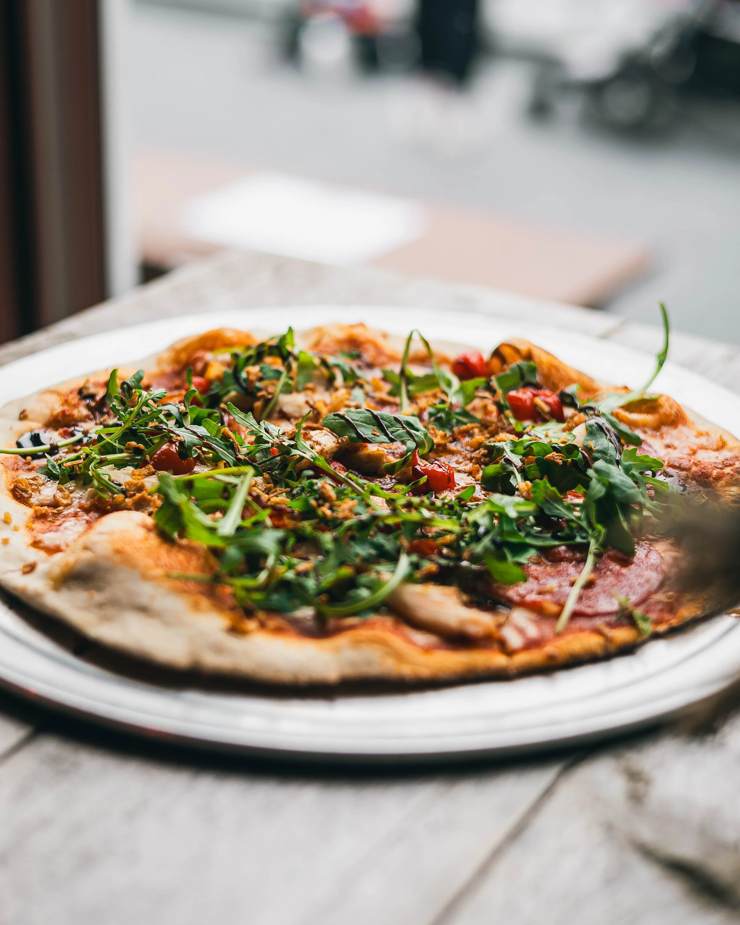 A fresh pizza topped with greens, red peppers, and various vegetables on a white plate.