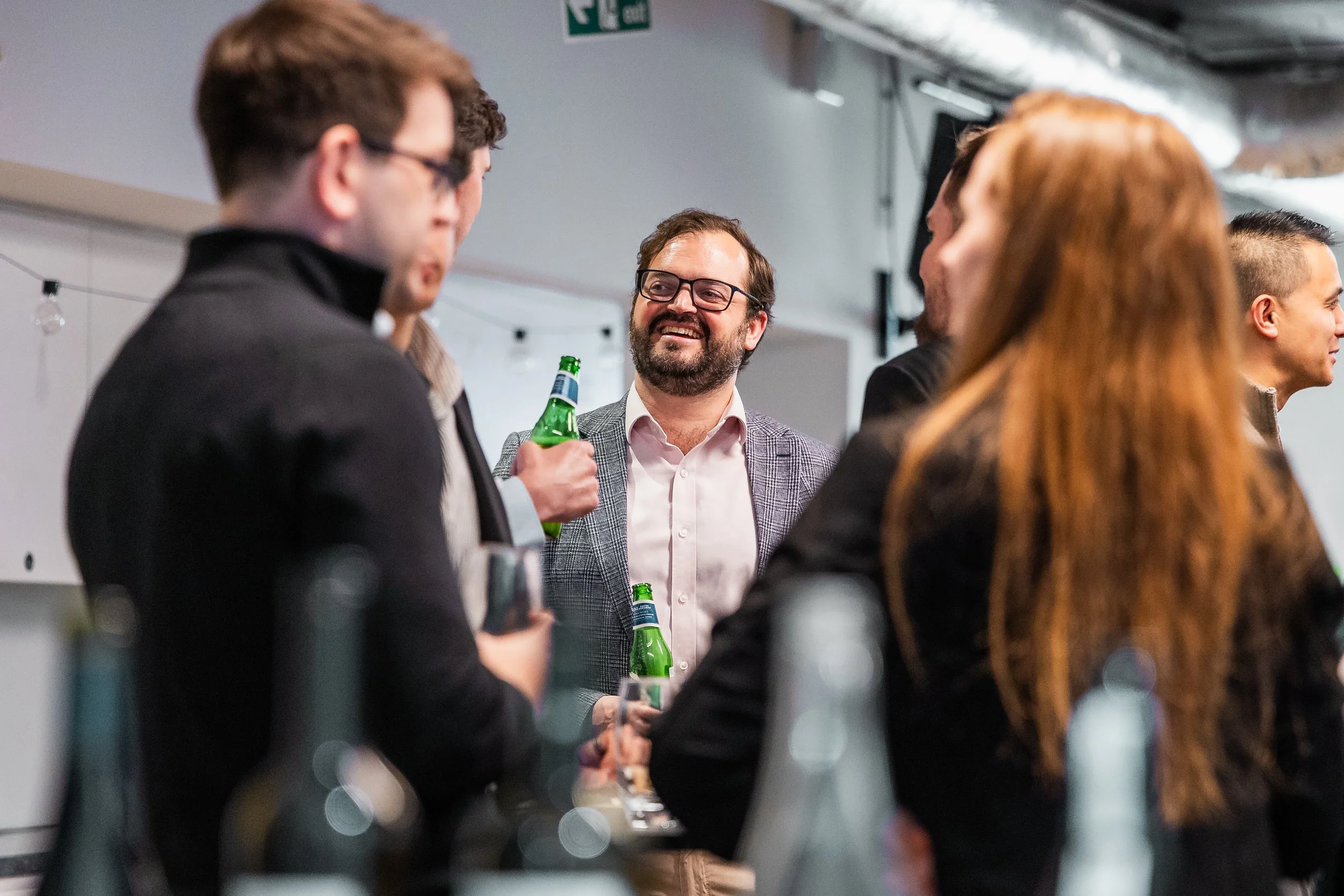 A man in glasses smiling while talking to someone at a business event by London Photographer Bobby Shoebotham