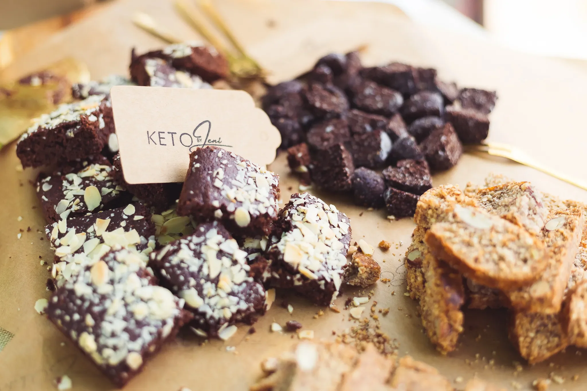Assorted brownie squares with toppings on a parchment paper, including chocolate, nuts, and shredded coconut, labeled 'KETO' in the center.
