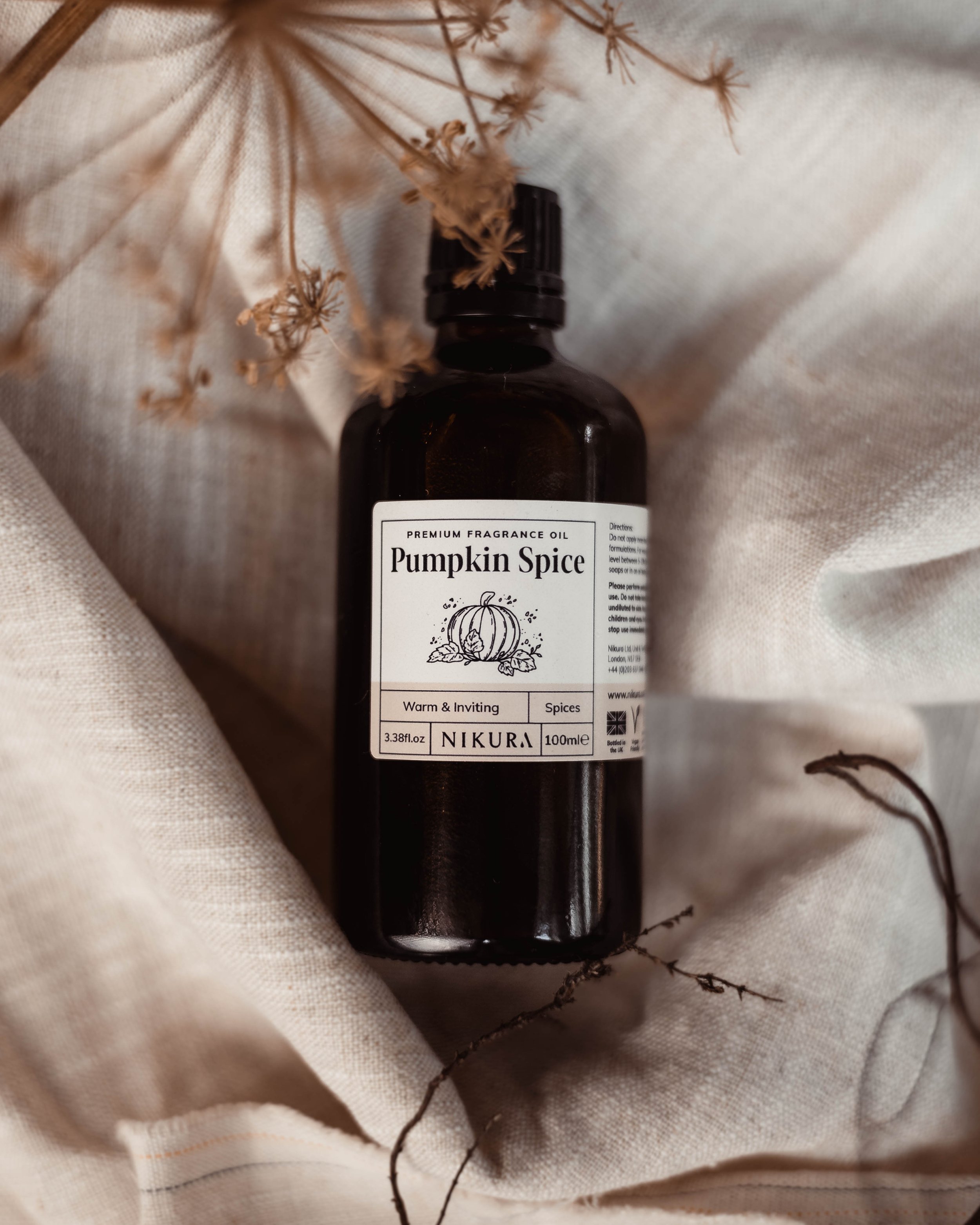A warm image of a pumpkin spice essential oil on some course beige linen with various twigs around it.