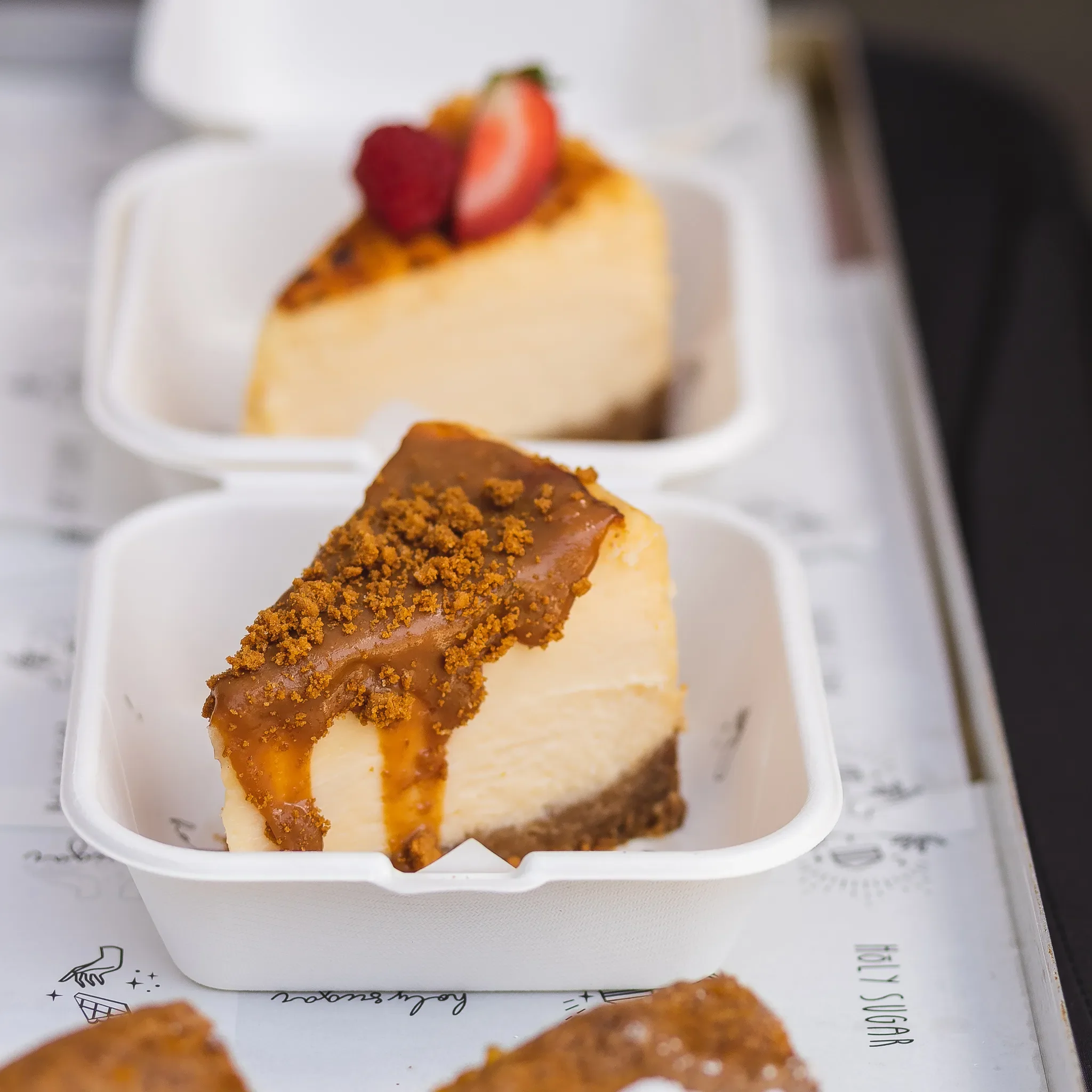 Two slices of cheesecake with different toppings in white containers