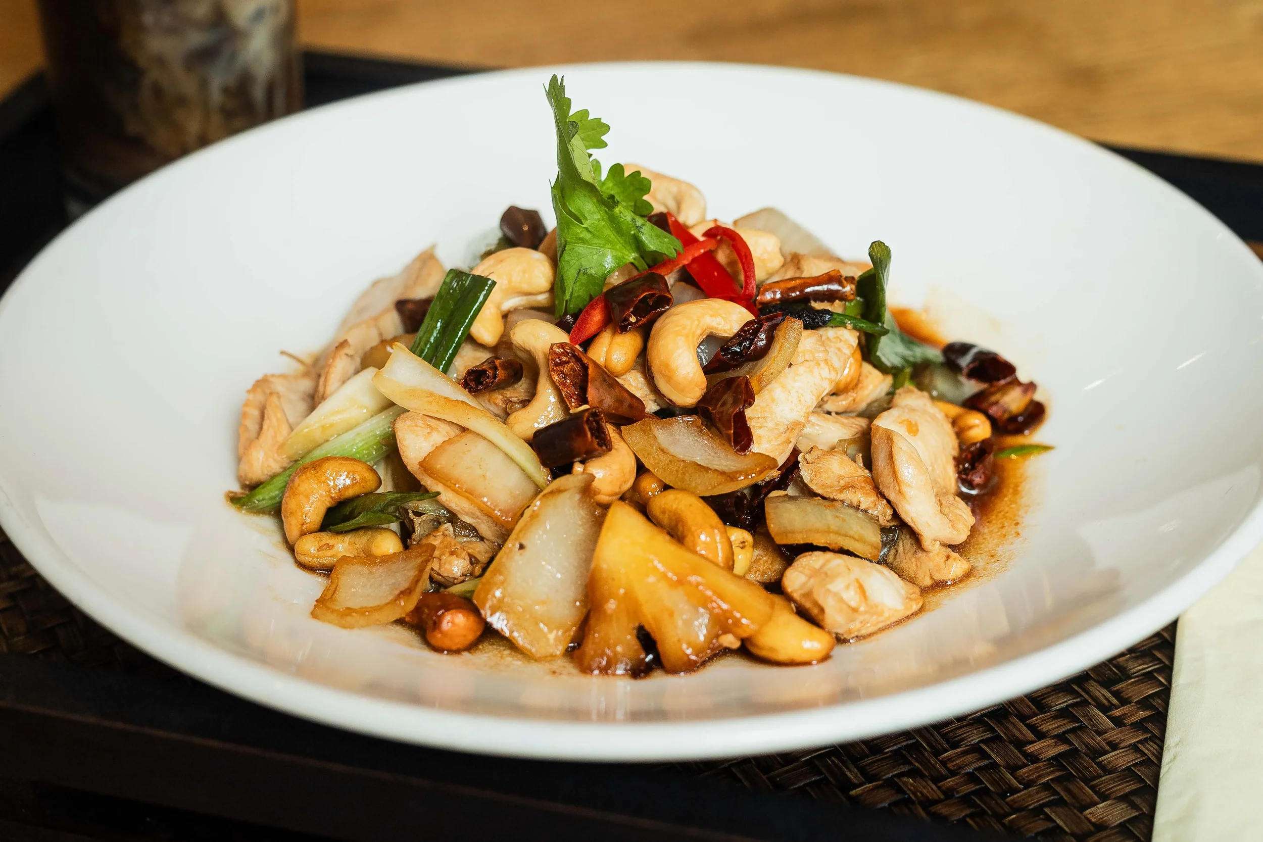 A plate of stir-fried chicken with cashews, onions, green onions, chili peppers, and fresh cilantro garnished on top.