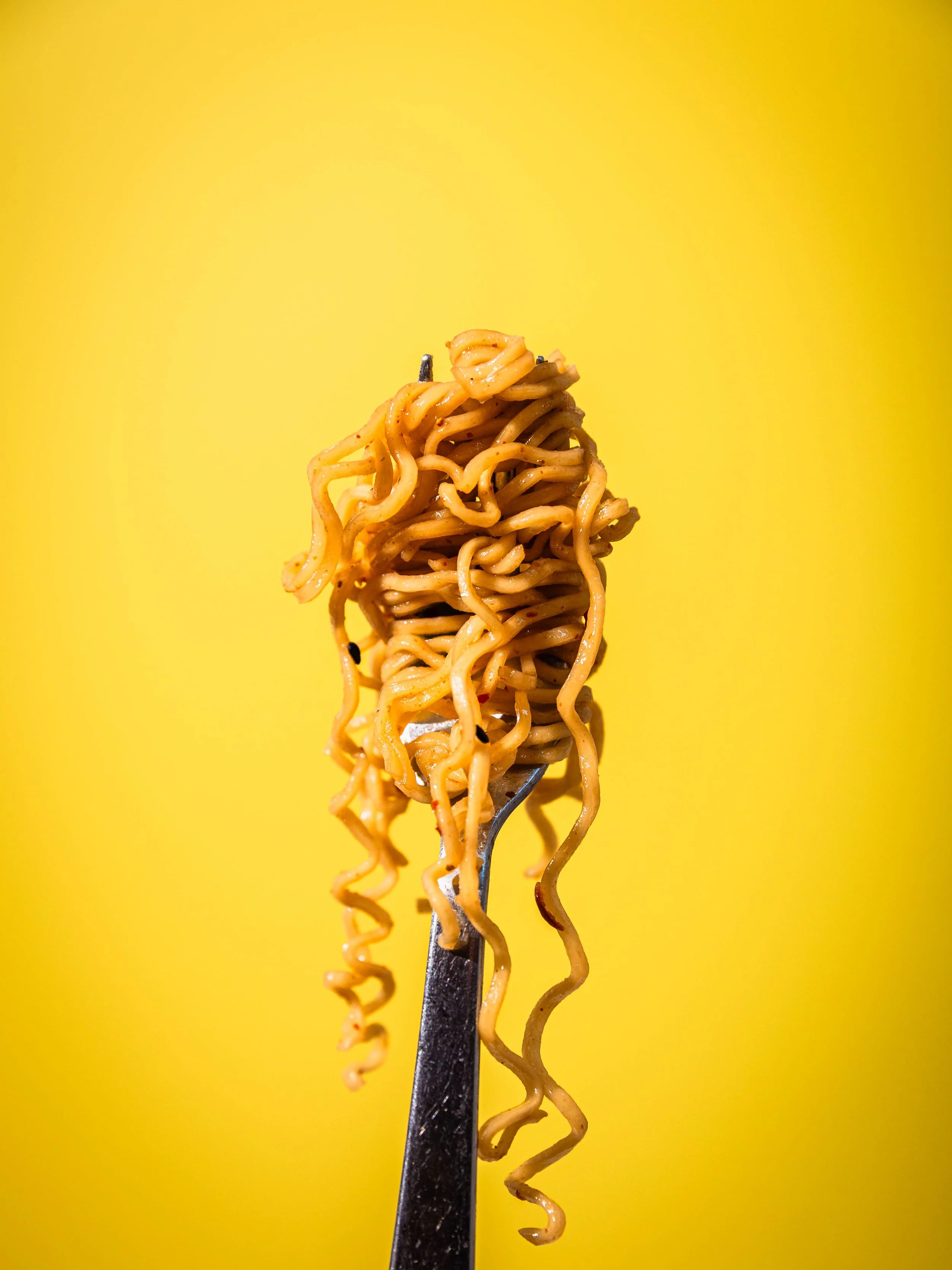 A fork with cooked instant ramen noodles against a bright yellow background.