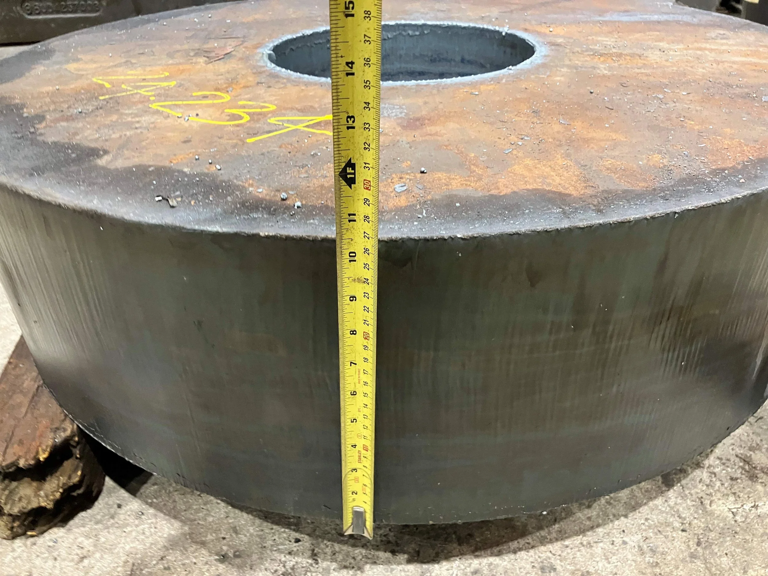 A large metal industrial component with a core hole and a tape measure showing approximately 14 inches in height.