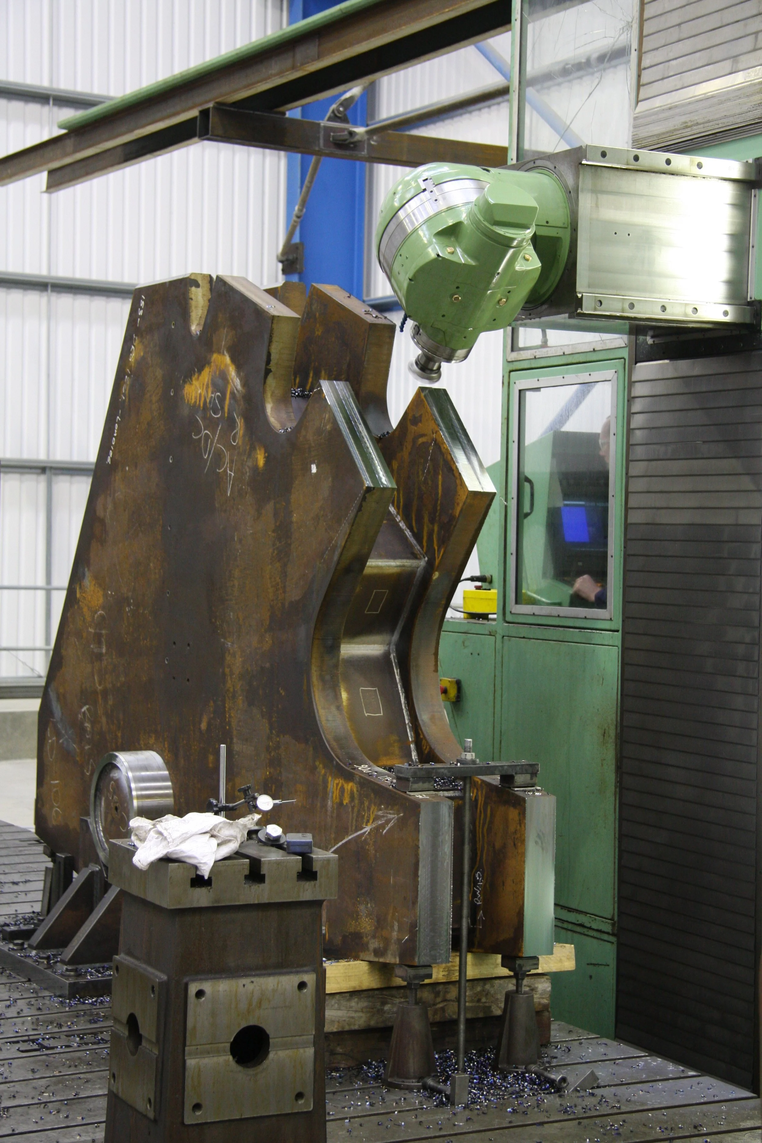A large, rusty metal component being machined with a CNC machine in an industrial workshop.