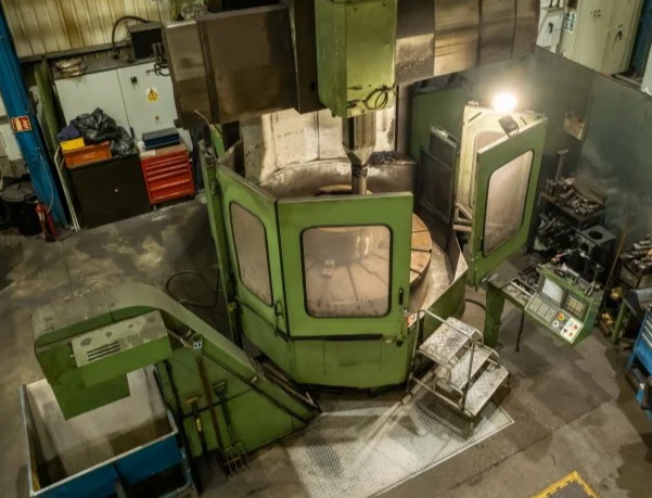Industrial CNC machine in a workshop with safety barriers and control panel.
