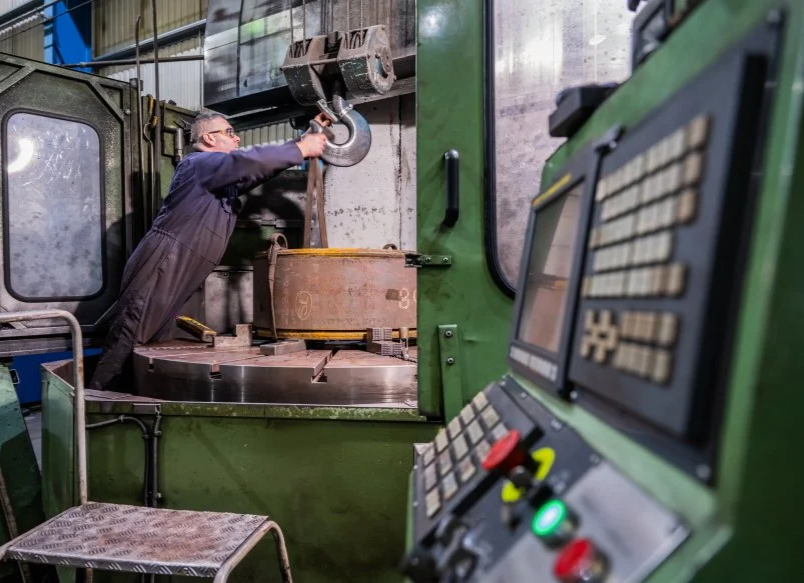 A man working inside a factory, operating a large green machining tool or CNC machine.