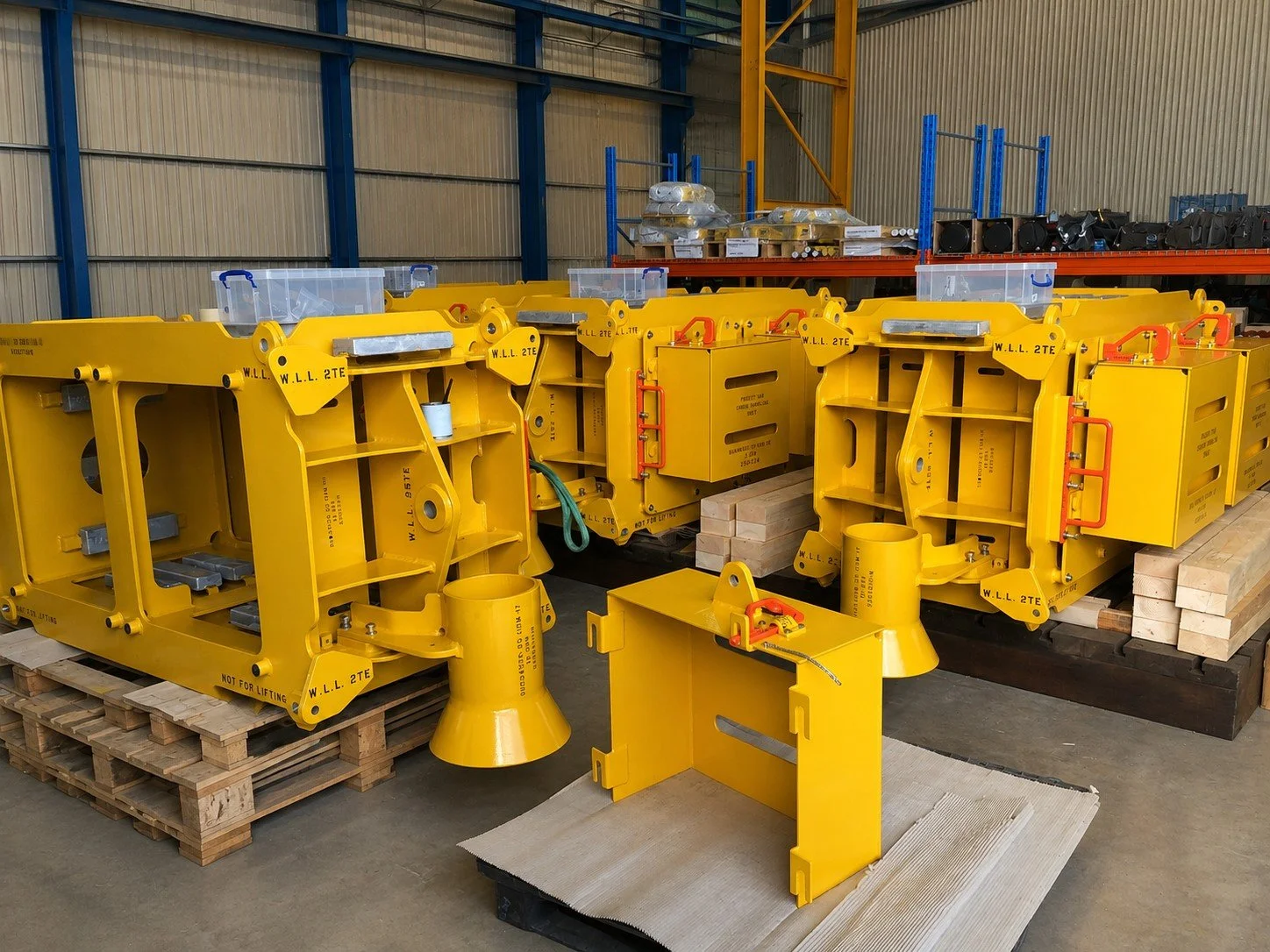Large yellow industrial machinery component in a workshop with tools, shelves, and workers in the background.