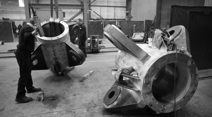 Workers assembling large industrial machine components in a manufacturing workshop.