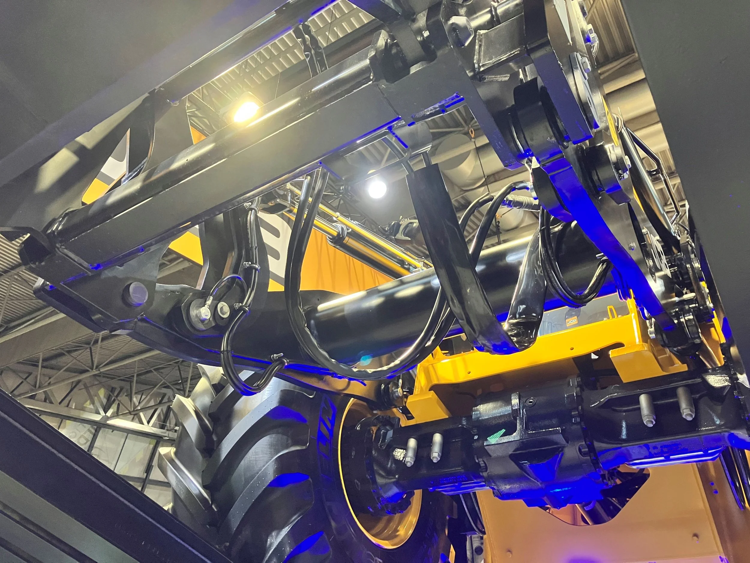 Large yellow industrial machinery component in a workshop with tools, shelves, and workers in the background.