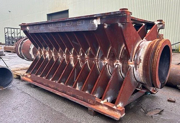 Large industrial metal crusher or grinder with a rusty exterior, positioned outdoors on a paved surface.