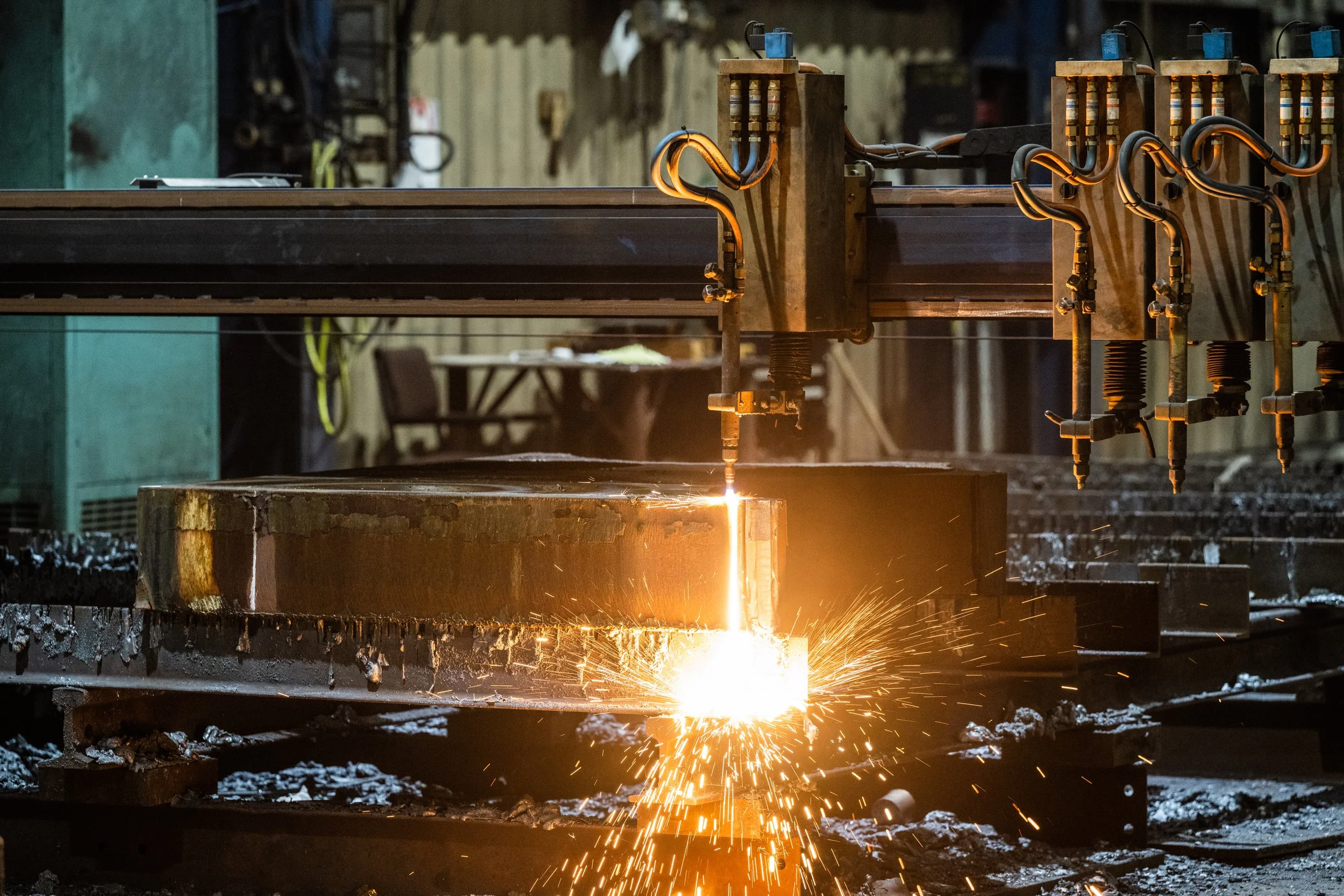 Industrial welding process with sparks flying as a metal piece is being cut or joined, with various welding equipment and tools in the background.