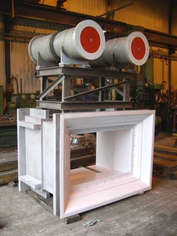 Large industrial air handling unit with two large cylindrical filters on top, housed in a metal frame with a large rectangular opening in a factory setting.