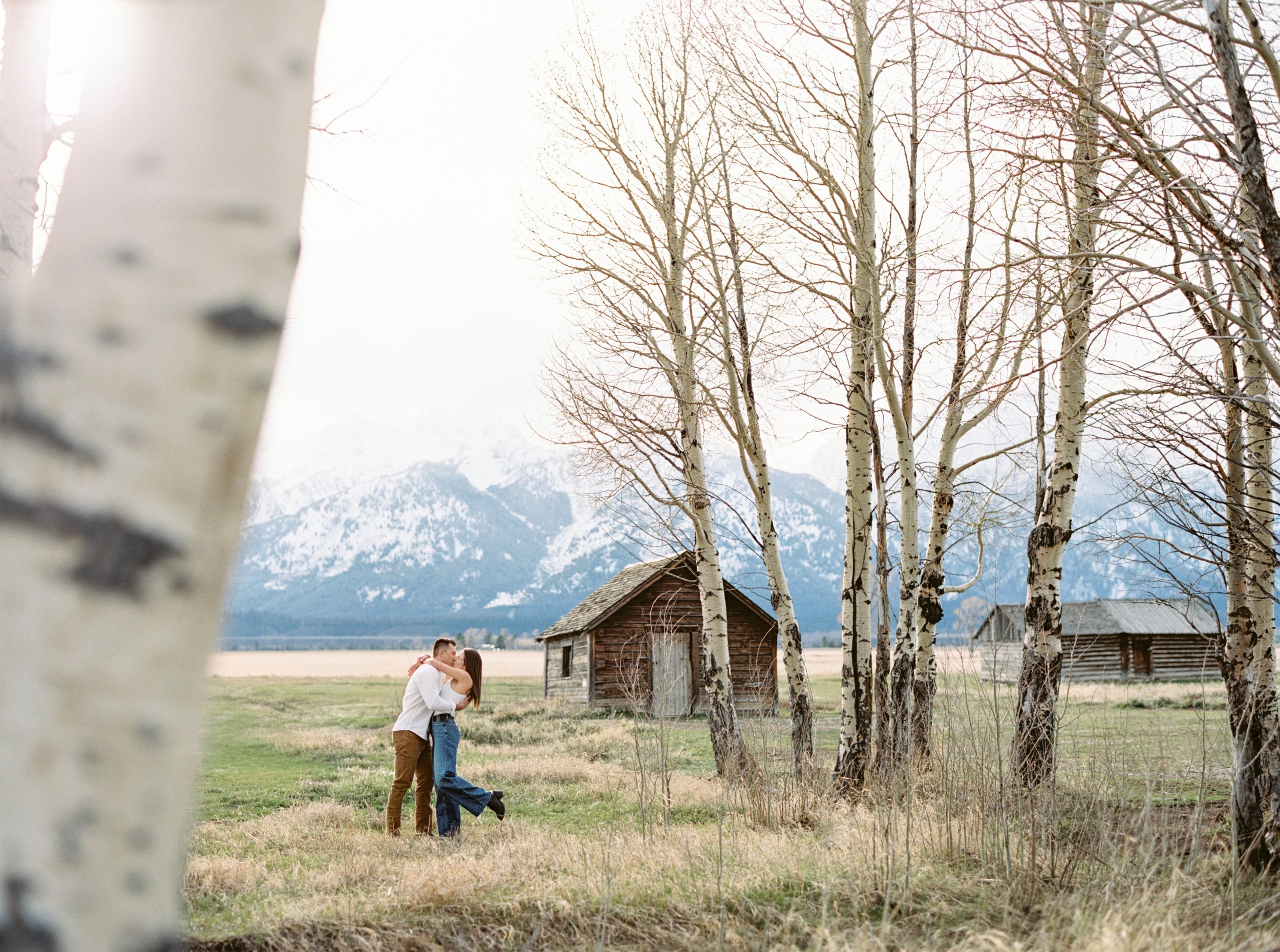 couple kissing by trees by Mormon Row in Grand Teton National park
