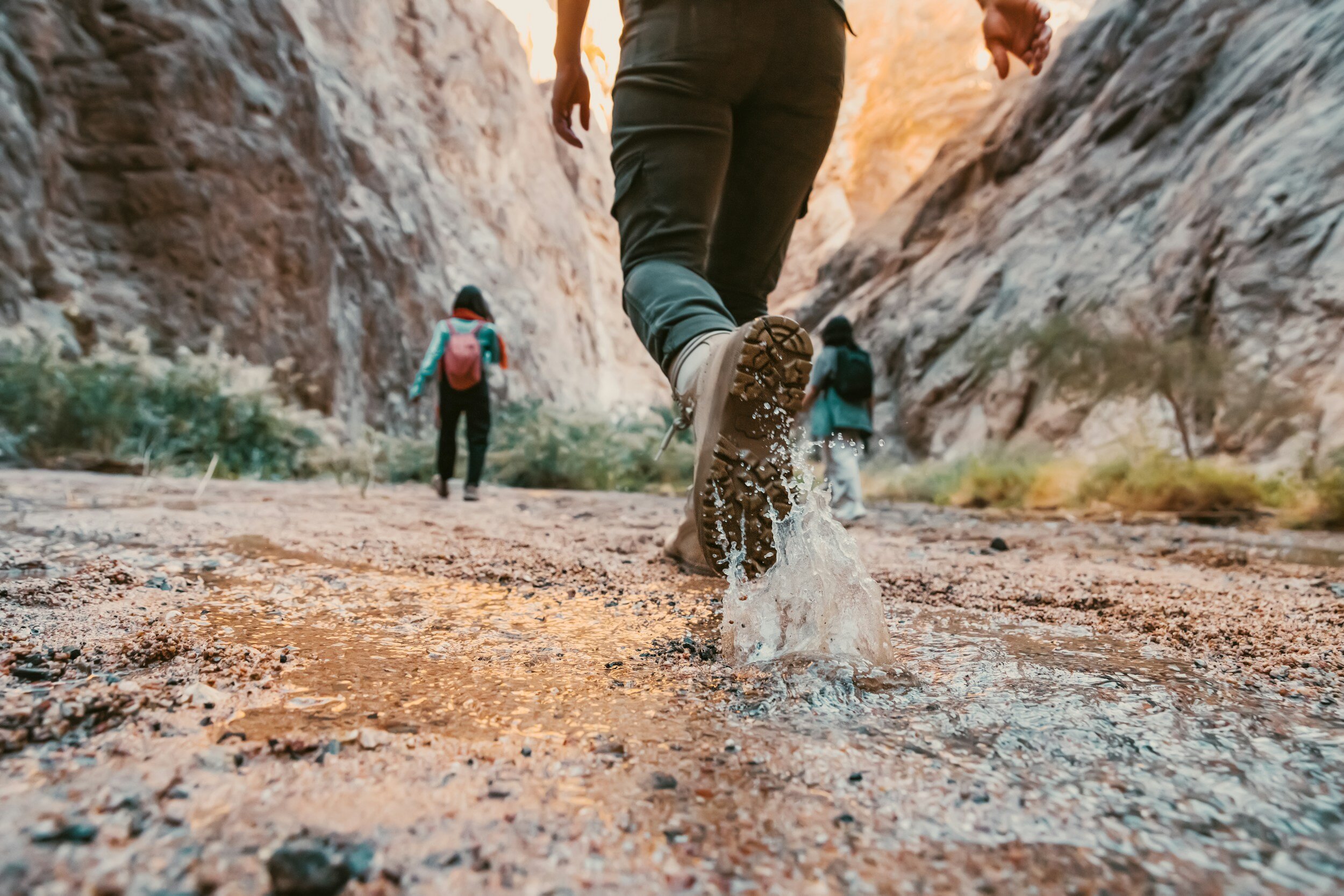 Hikers walking through a narrow canyon with water splashing underfoot.