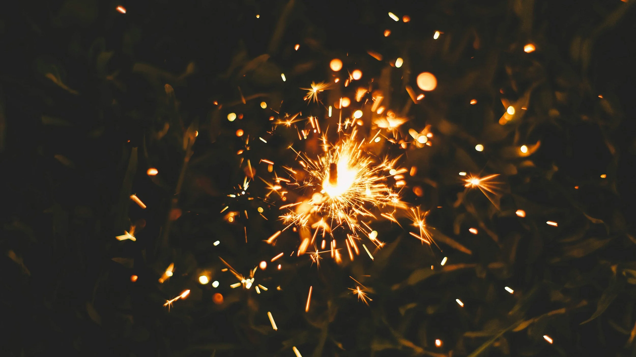 A close-up of a lit sparkler emitting bright sparks against a dark background.