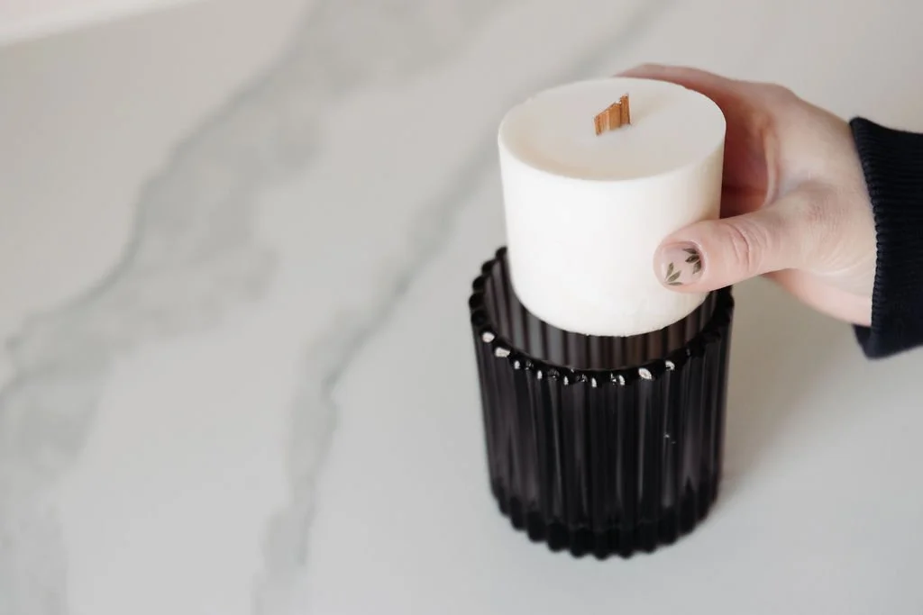 A white candle on top of a gold box labeled 'August Moon Rise candle refill,' with two similar boxes stacked beside it on a wooden surface.