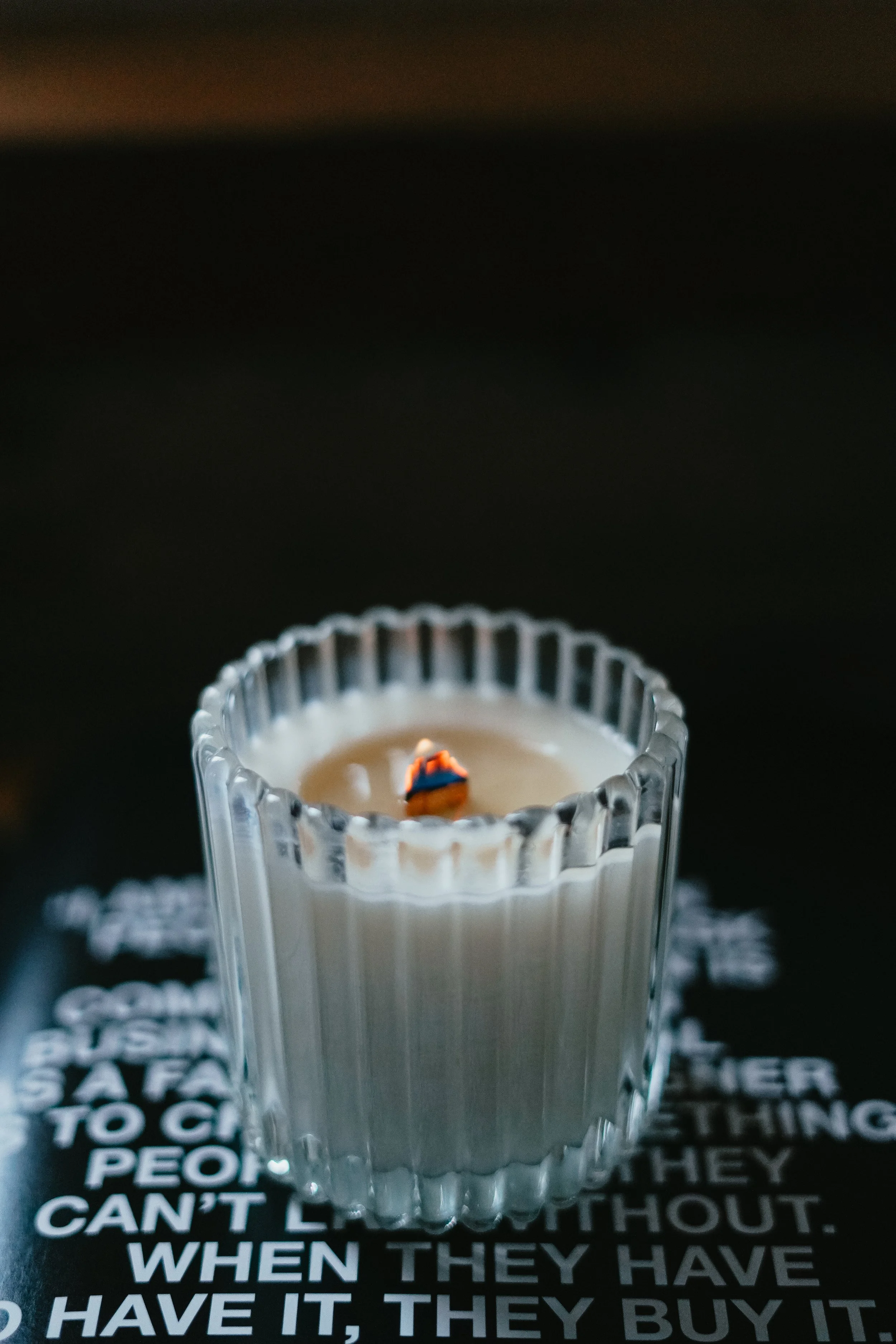 Person in brown shirt holding lit candle in brown glass holder.