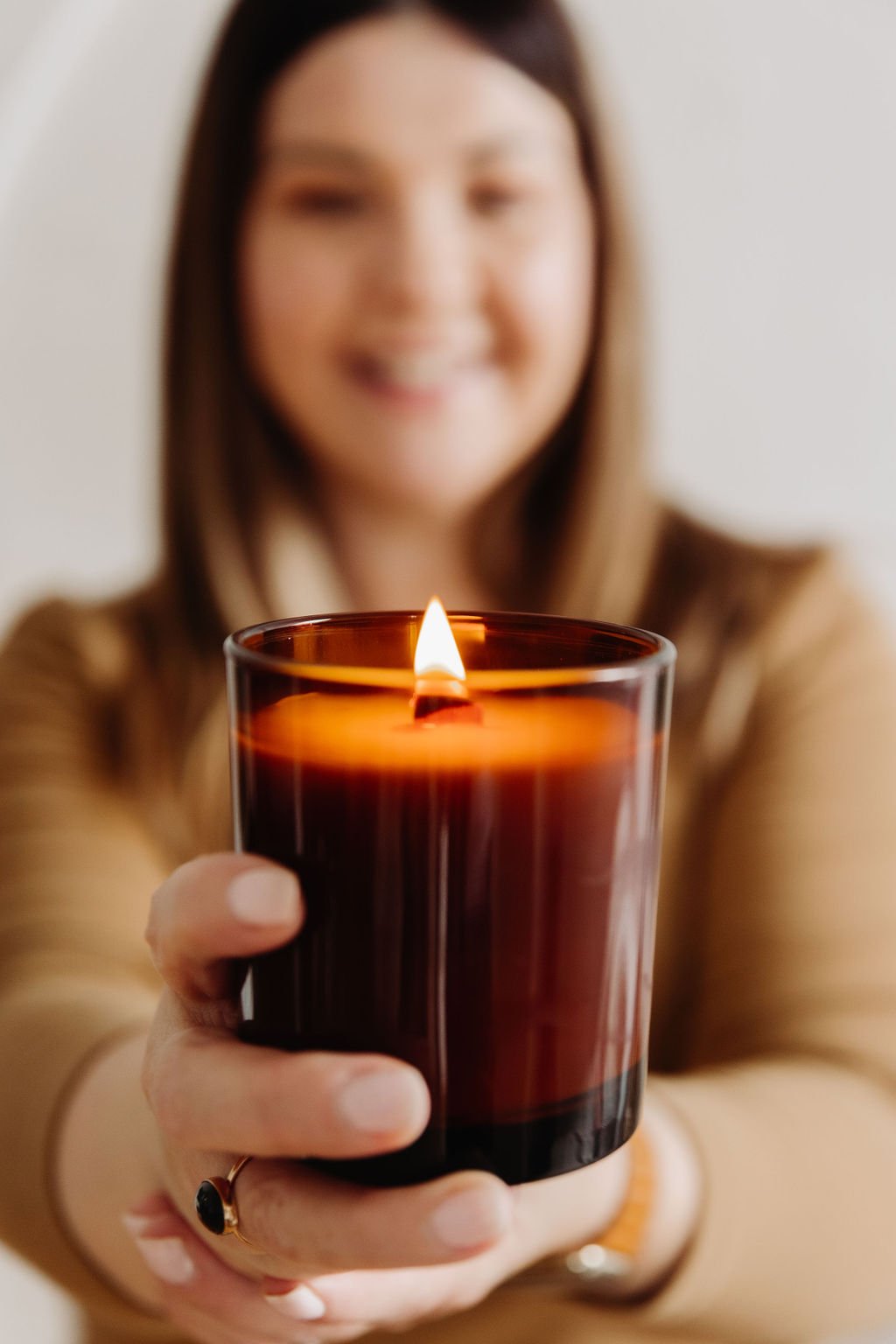 A blurry woman holding a lit candle in a brown container, focus on the candle.