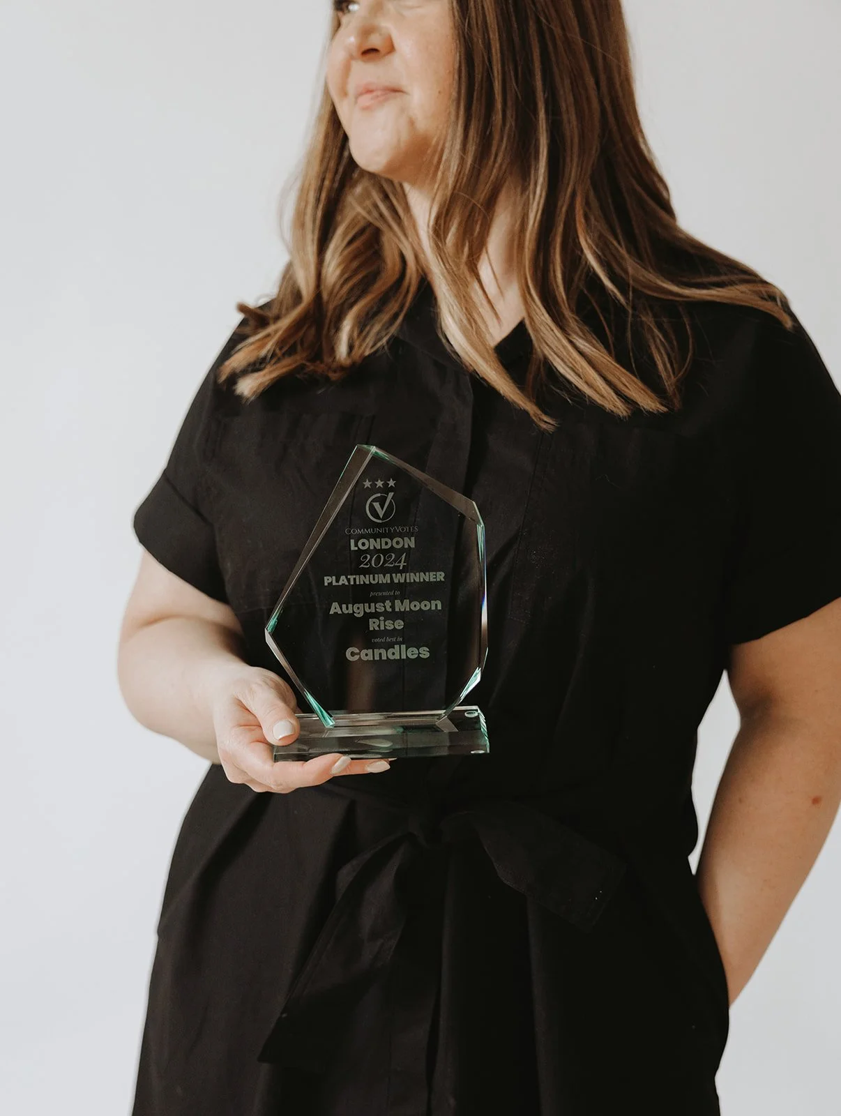 Woman holding a glass award for "Community Votes London 2024 Platinum Winner August Moon Rise Candles."