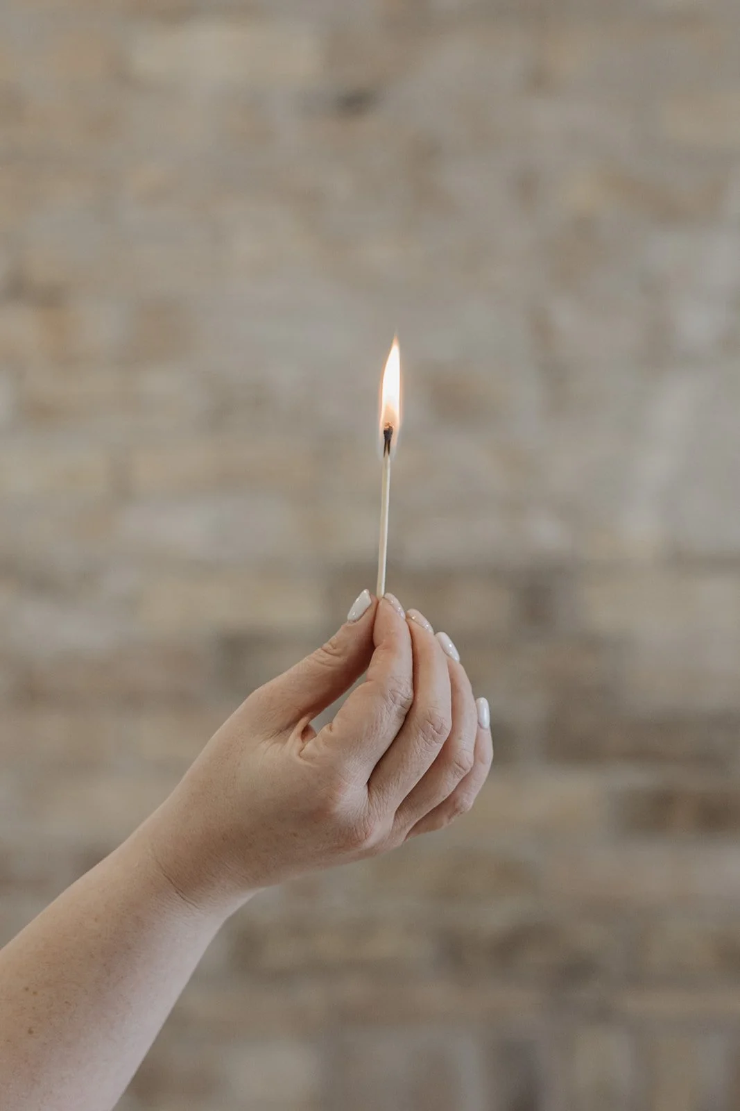 Lit candle in a glass holder on a table, person sitting cross-legged in the background holding a coffee cup.