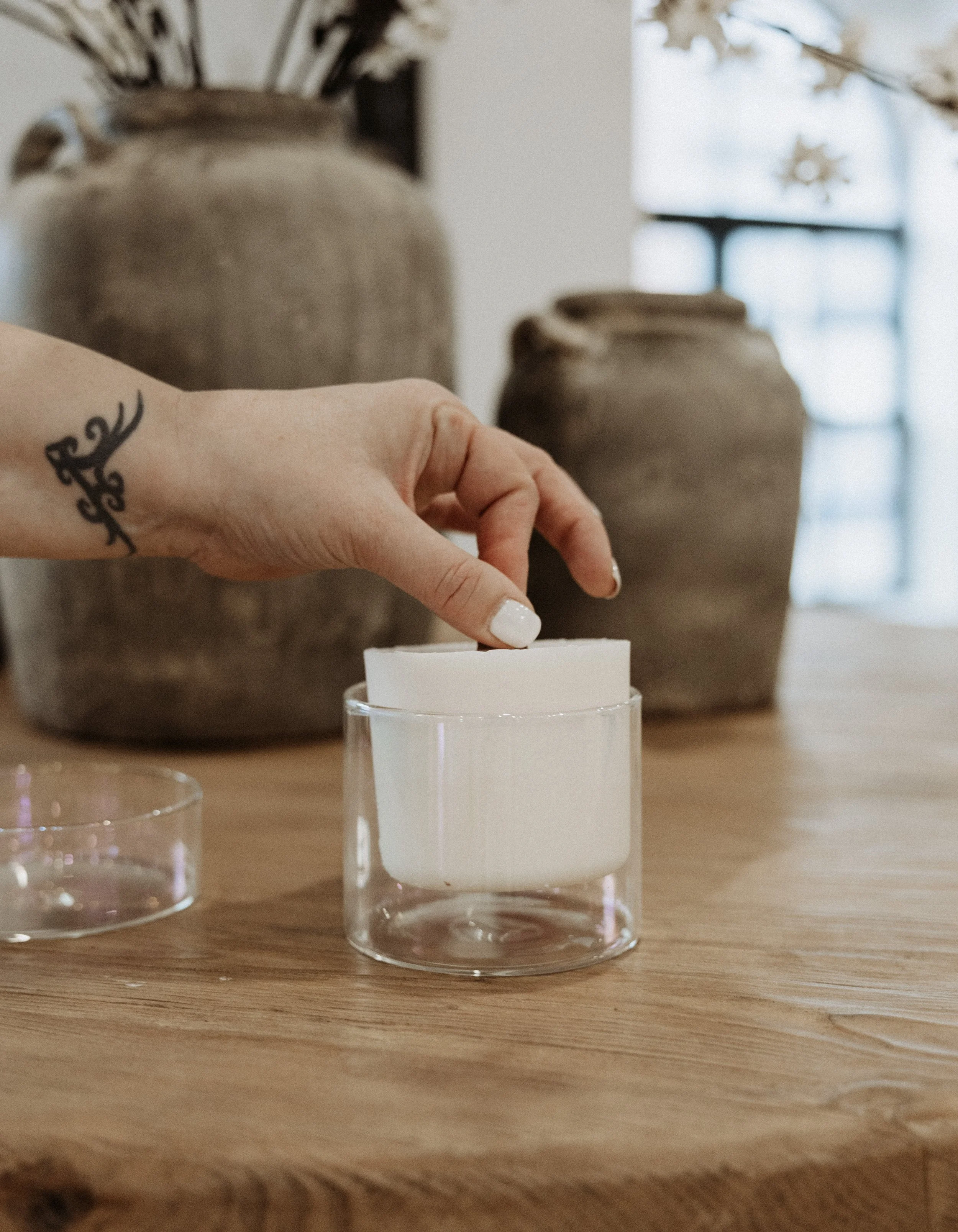 A white candle on top of a gold box labeled 'August Moon Rise candle refill,' with two similar boxes stacked beside it on a wooden surface.