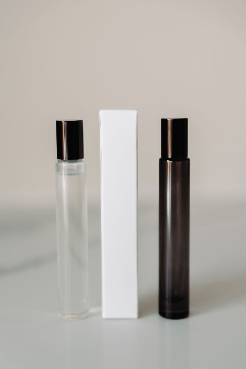 Two glass bottles with black caps and a white rectangular box in between, against a plain background.